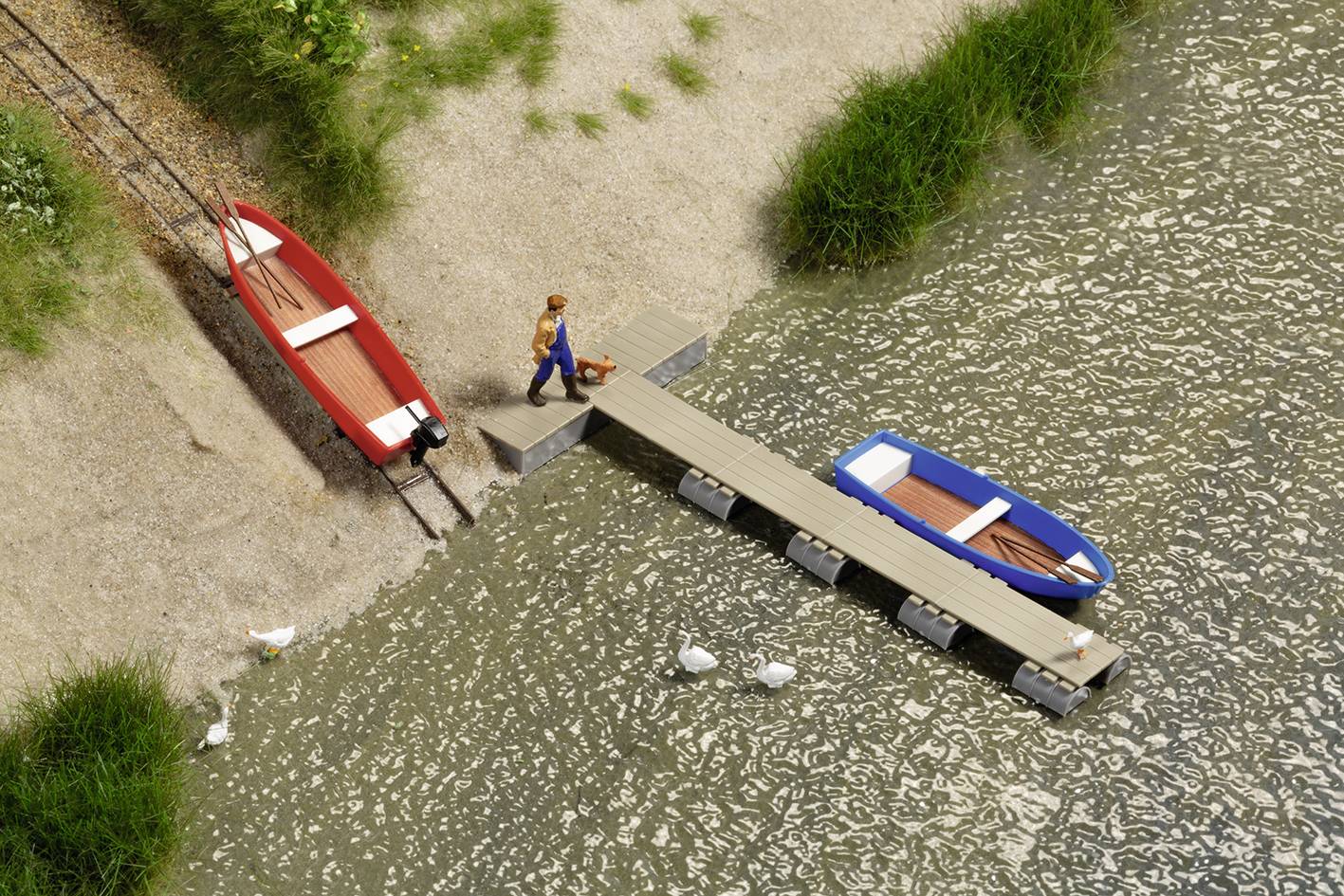 Ein Miniaturmodell zeigt einen Mann auf einem Steg zwischen zwei Booten, umgeben von Wasser und Gras. Drei Enten schwimmen im Wasser.