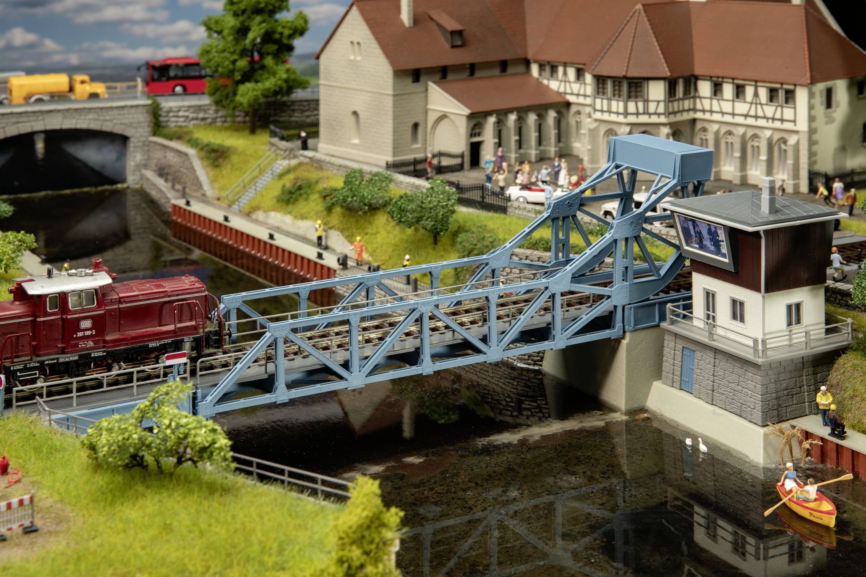 Miniatureisenbahn-Diorama mit beweglicher Brücke, Zug, detaillierten Gebäuden und Landschaft. Szene wirkt realistisch und lebendig.