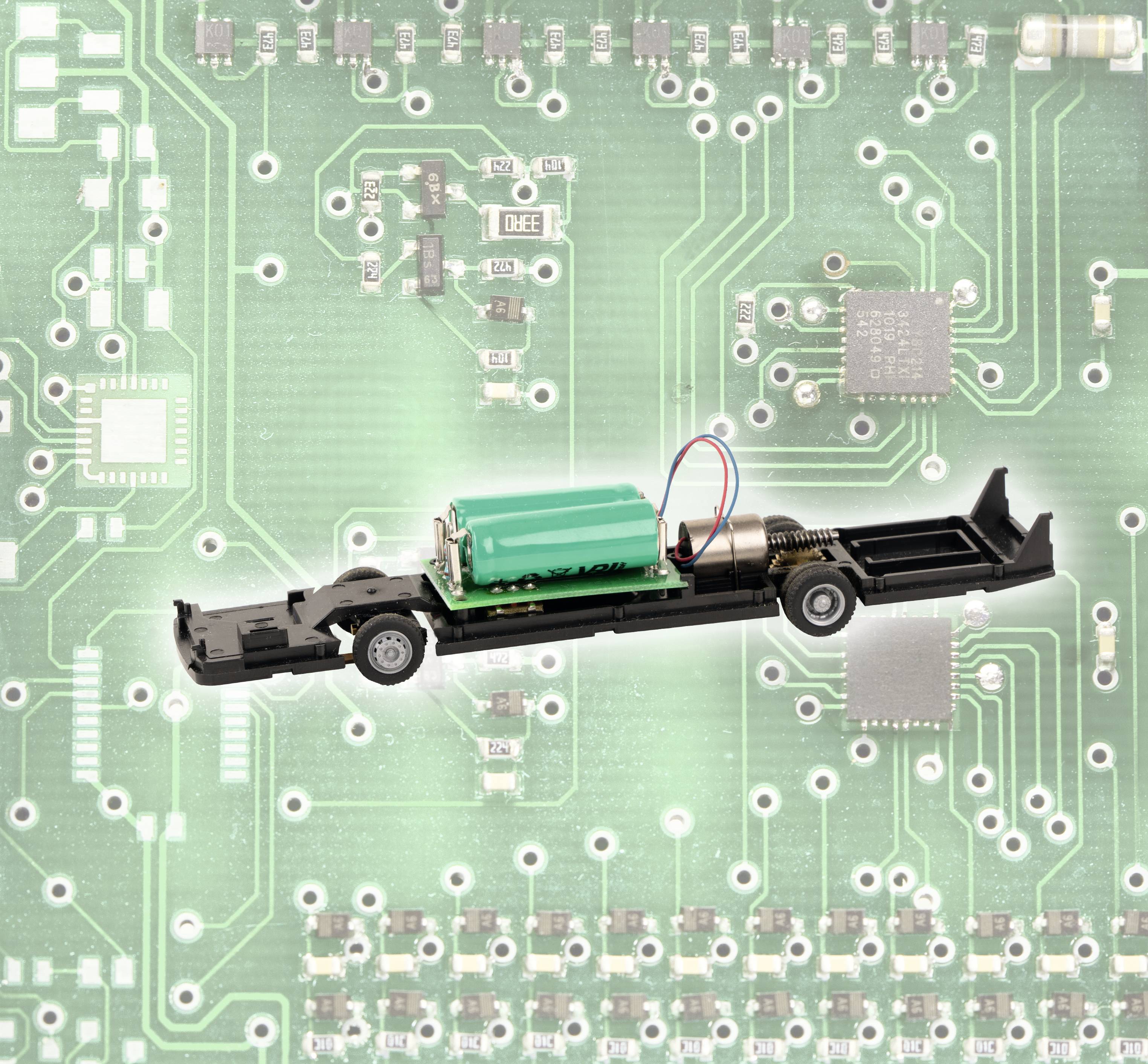 Ein kleines Modell eines Elektrofahrzeugs mit Batterie und Motor ist auf einer vergrößerten grünen Leiterplatte positioniert.
