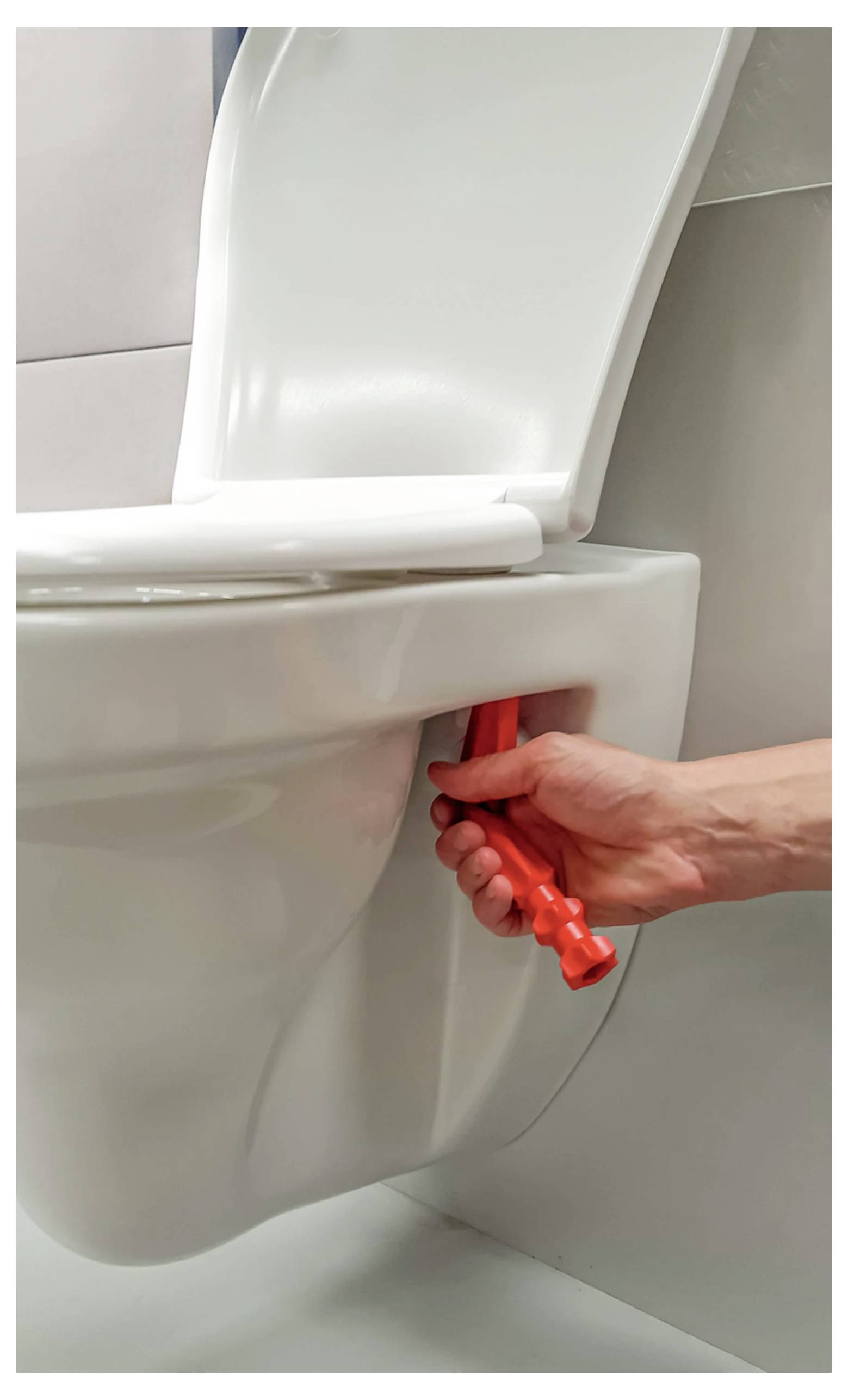 Eine Hand, die ein rotes Werkzeug hält, justiert die Unterseite eines weißen Toilettensitzes, höchstwahrscheinlich für Installations- oder Wartungszwecke.