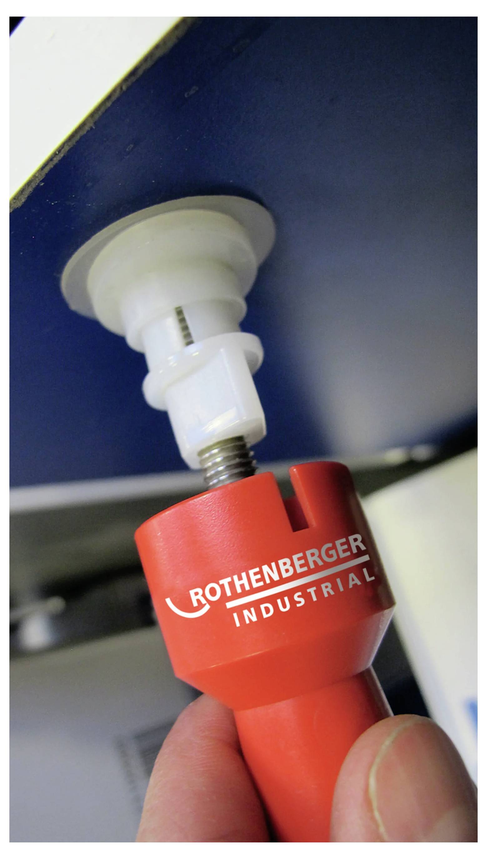 Ein rotes 'ROTHENBERGER INDUSTRIAL' Werkzeug, das verwendet wird, um eine Armatur unter einem Waschbecken zu lösen oder anzuziehen, wobei der Fokus auf der Interaktion des Werkzeugs mit dem Teil liegt.