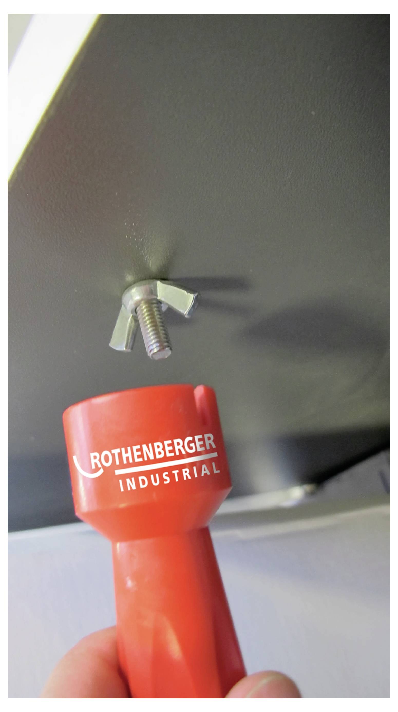 Ein roter Rothenberger Industriewerkzeug wird verwendet, um eine Flügelmutter an einem Bolzen festzuziehen.