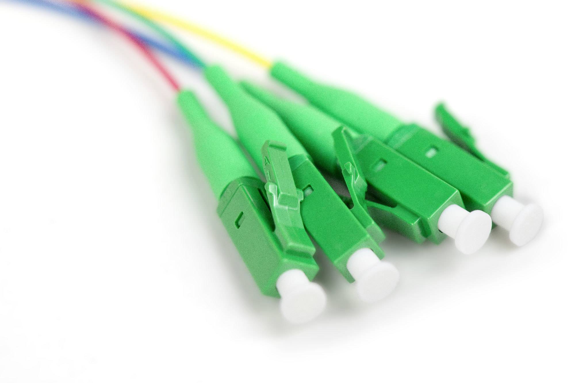 Vier grüne Glasfaserkabelstecker, nebeneinander liegend, mit farbigen Kabeln. Sie sind bereit zur Verbindung und Datenübertragung.