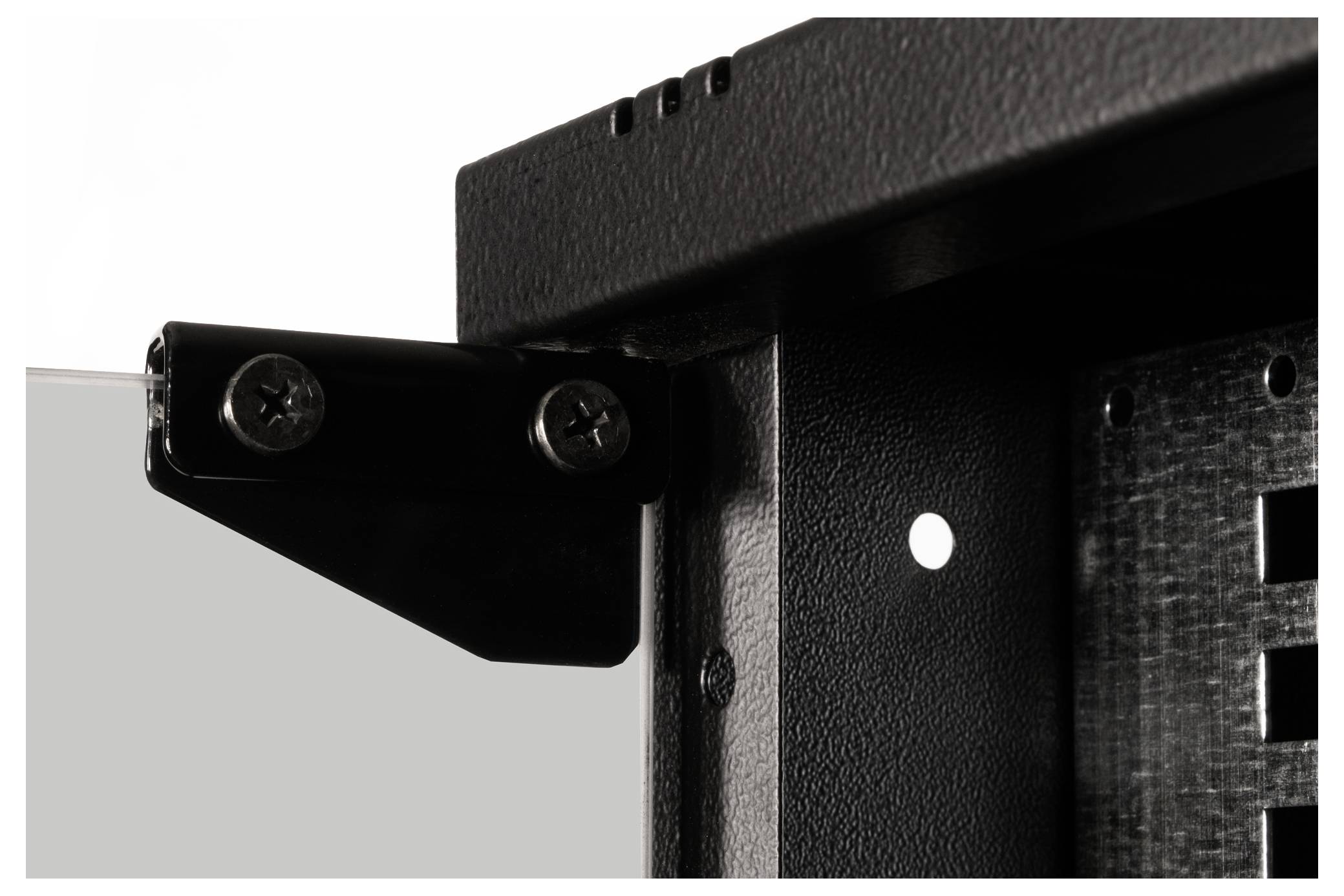 Nahaufnahme eines schwarzen Metallwinkels, der mit zwei Schrauben an der Ecke eines Rahmens befestigt ist.