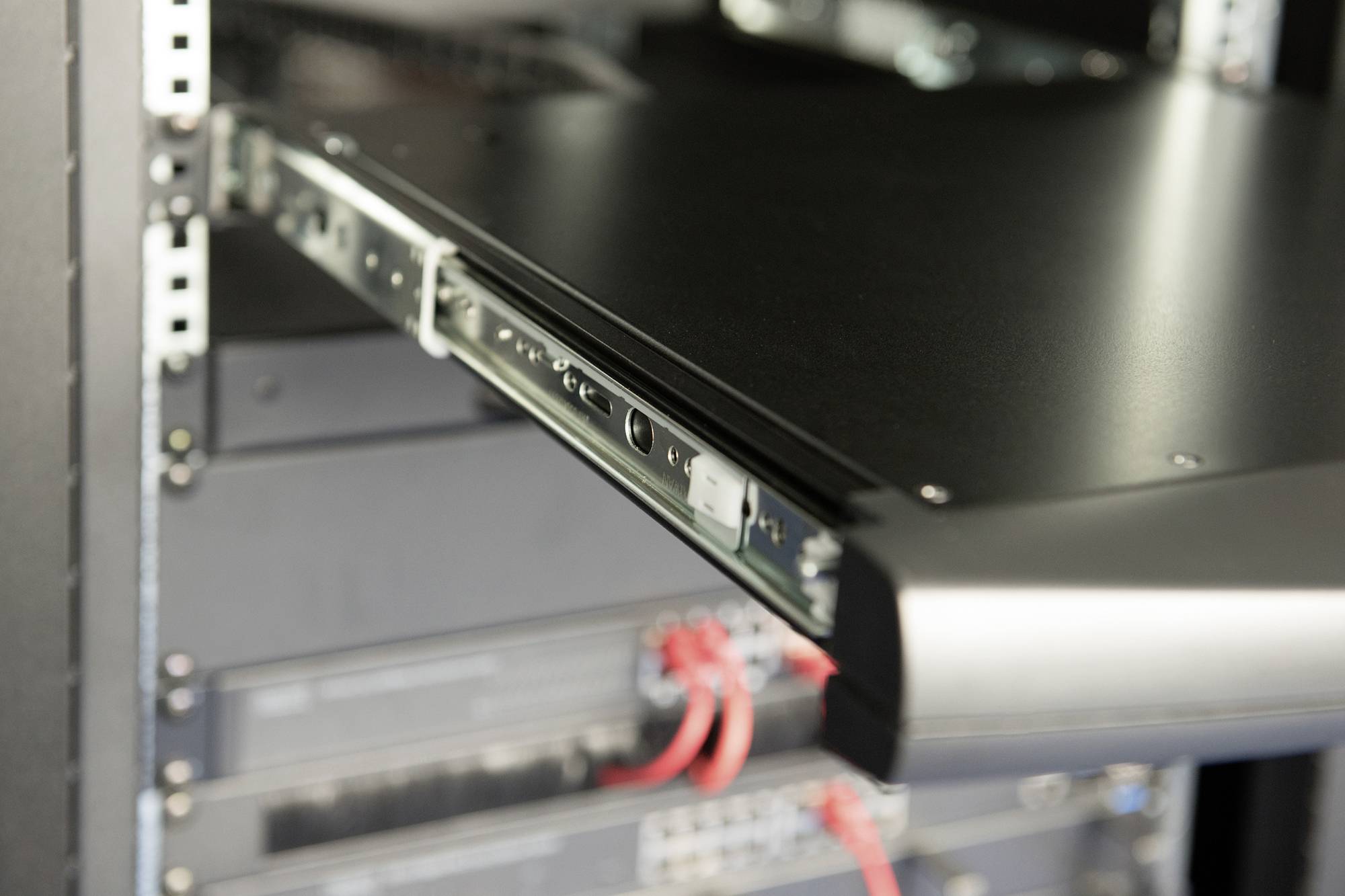 Ein Server-Rack mit herausgezogener Schublade in einem Rechenzentrum. Kabel und Geräte sind sichtbar, umgeben von einem metallischen Rahmen.