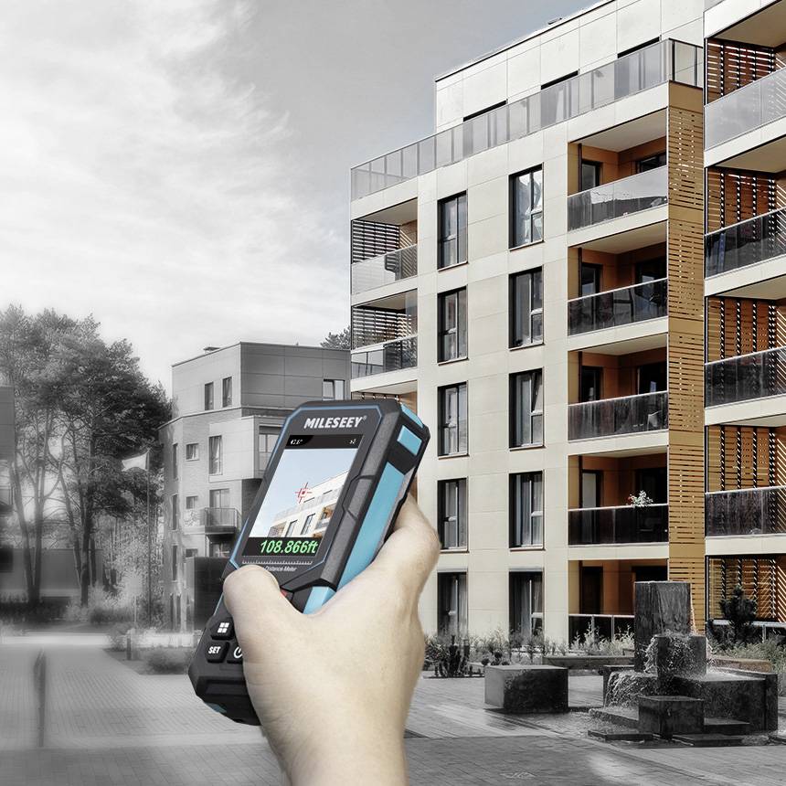 Eine Hand hält ein digitales Messgerät vor einem modernen Wohngebäude mit mehreren Etagen.