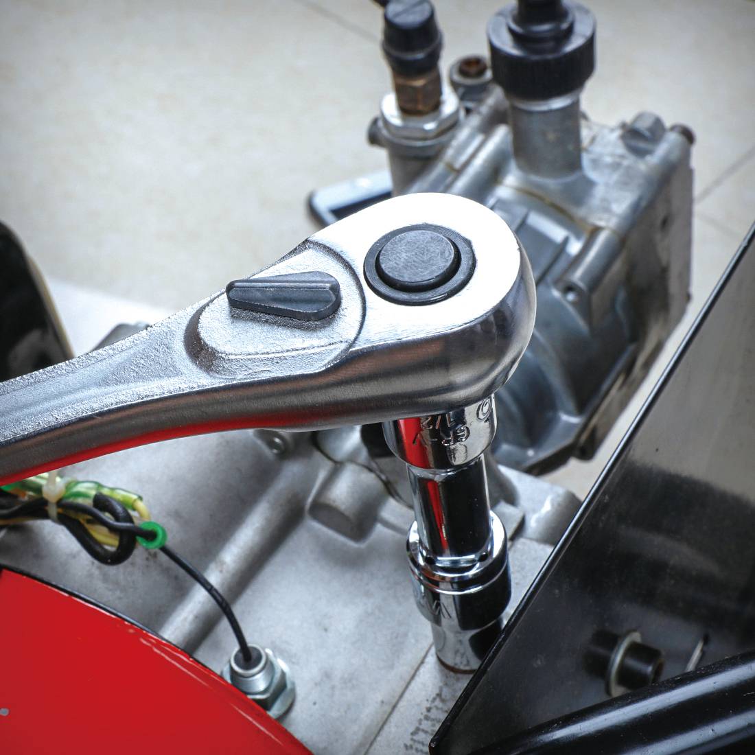 Nahaufnahme eines Steckschlüssels, der eine Mutter löst oder festzieht. Im Hintergrund ist ein Maschinenmotor sichtbar.