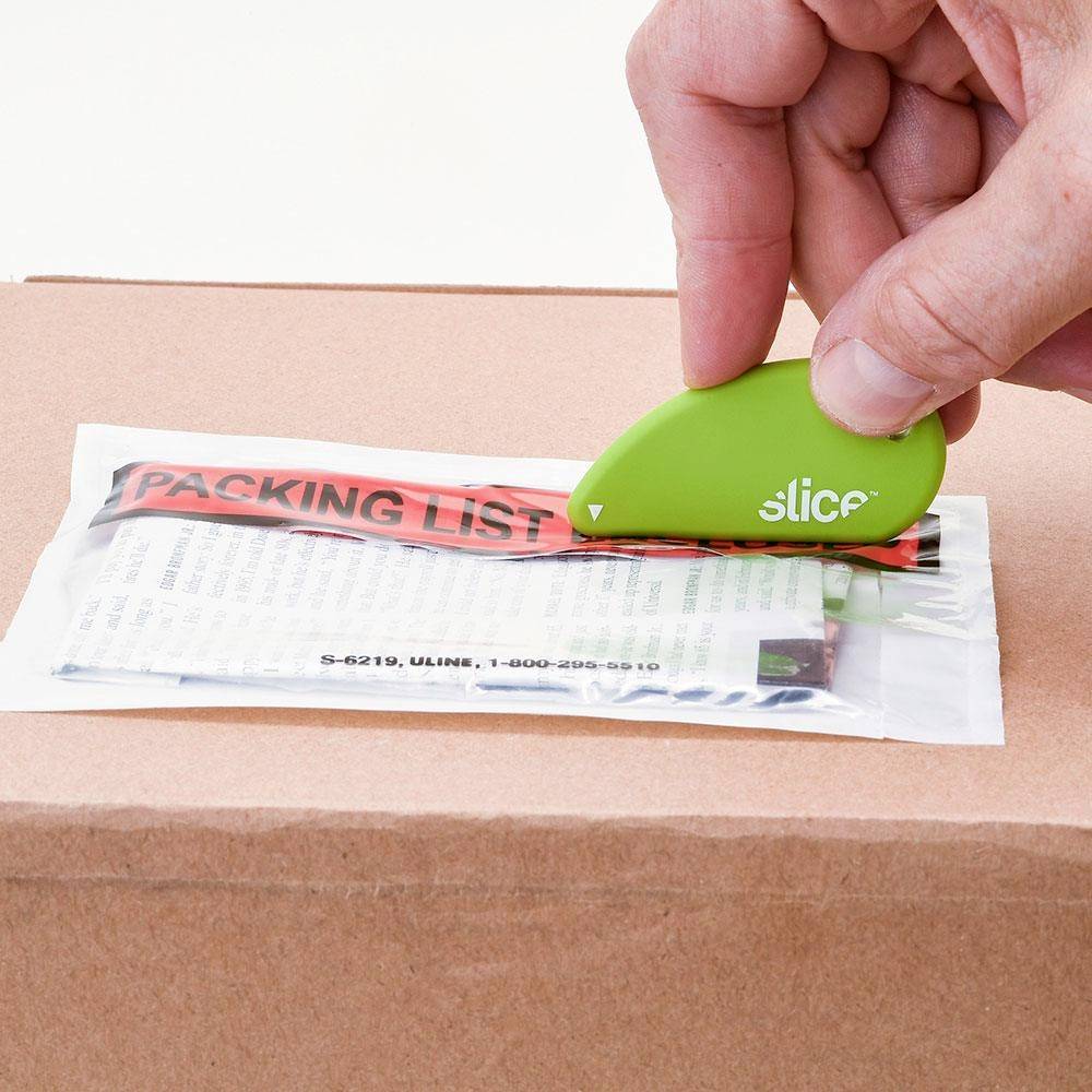 Eine Hand verwendet einen kleinen, grünen 'slice'-Schneider, um ein Packband auf einem Karton entlang einer roten Packliste zu öffnen.