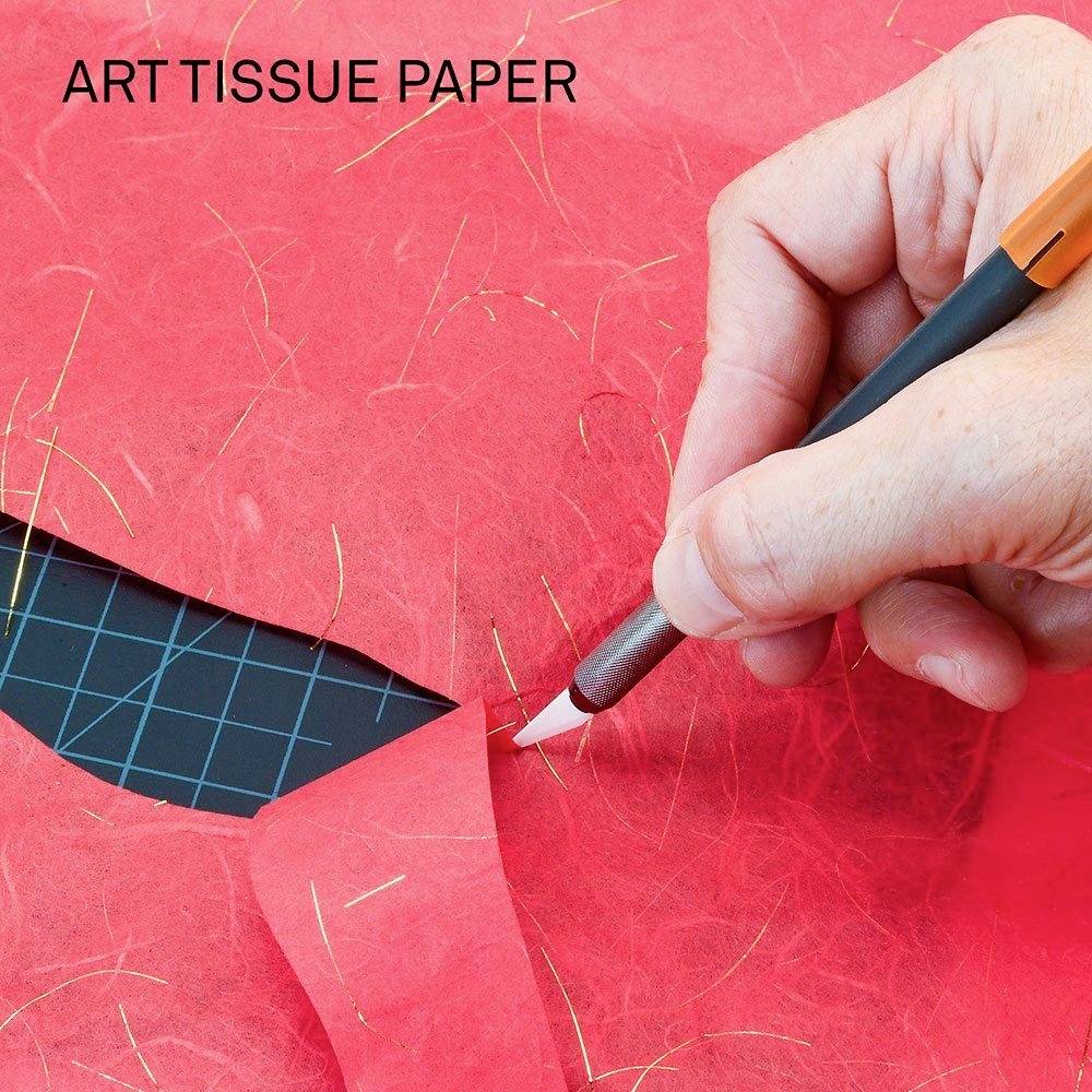 Hand schneidet mit einem Cutter-Messer rotes Papier, auf welchem 'ART TISSUE PAPER' steht.