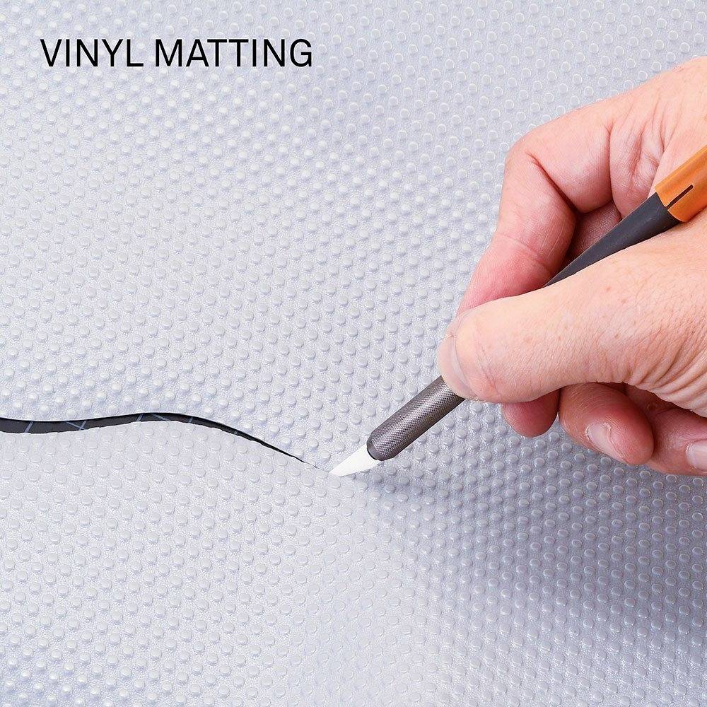 Eine Hand schneidet mit einem Messer einen schwarzen Streifen in eine graue Vinylmatte.