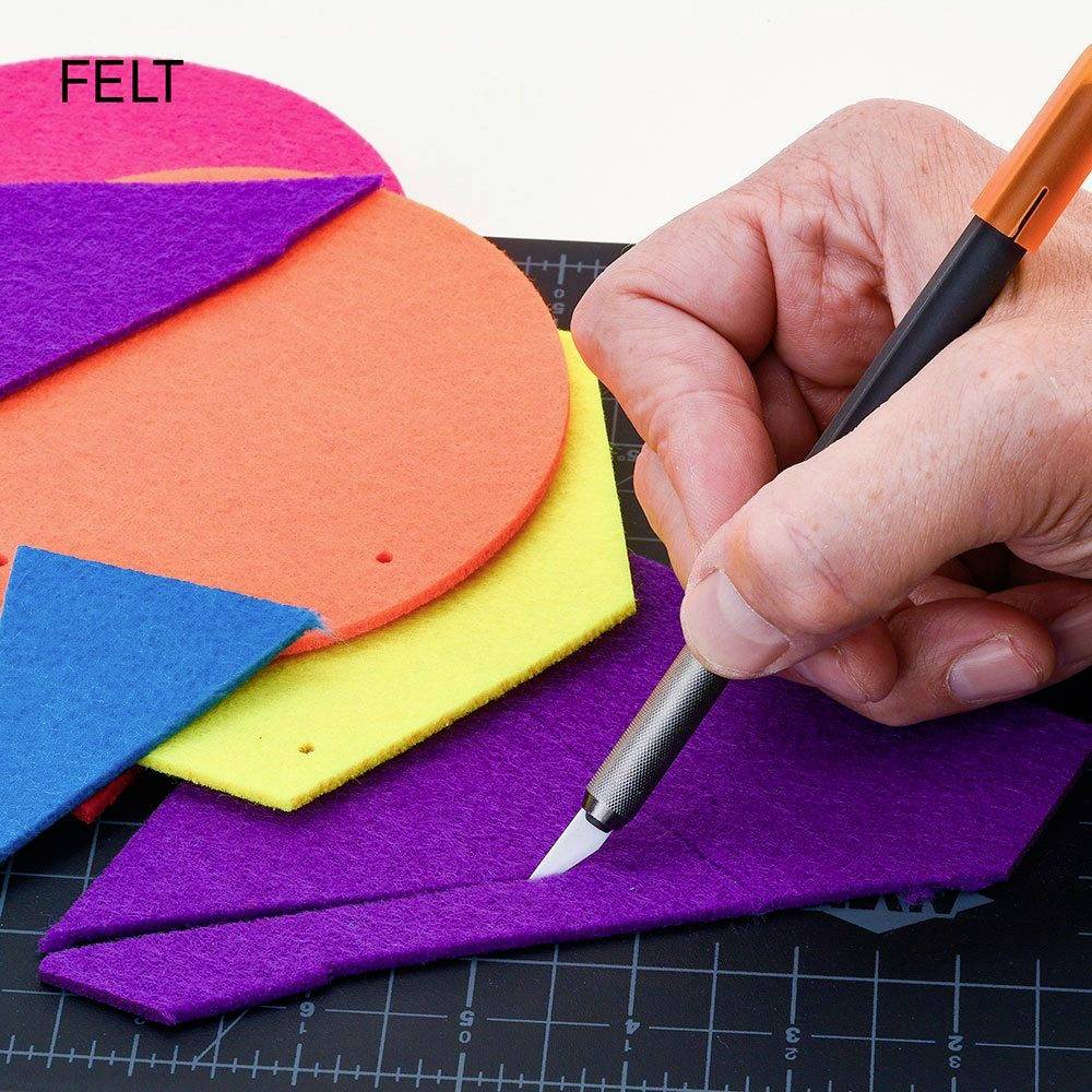 Ein Hand schneidet violetten Filz mit einem Stiftmesser auf einem Lineal-Schnittbrett. Bunte Filzstücke im Hintergrund.