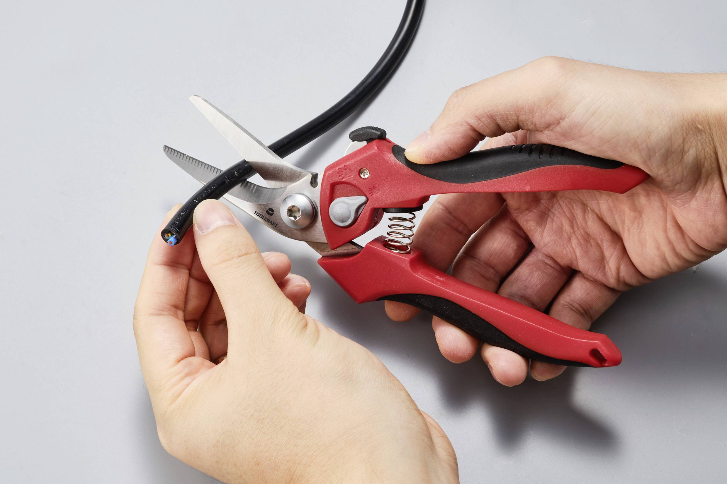 Person schneidet ein schwarzes Kabel mit einer roten Kabelschere.