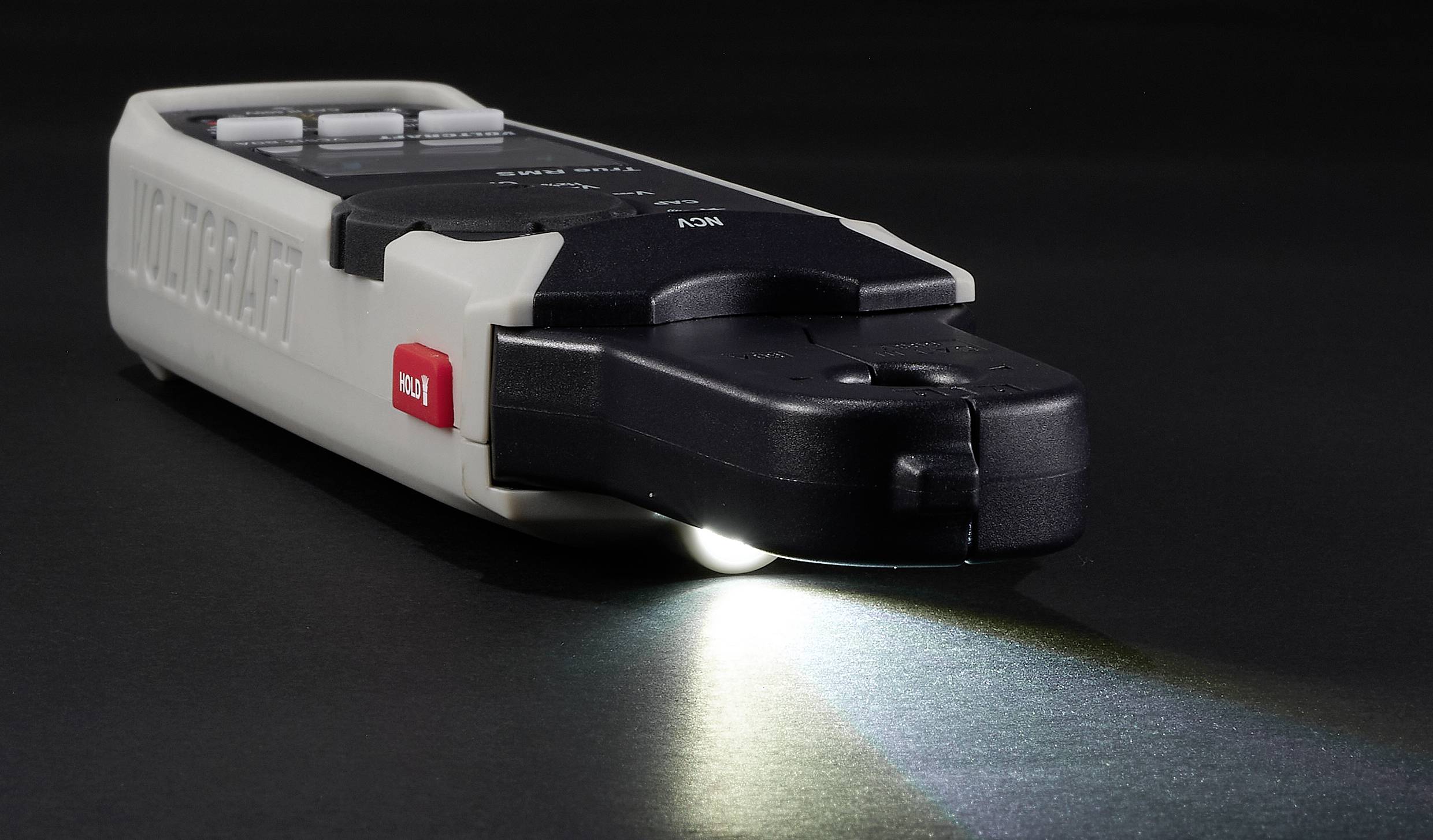 Ein handgehaltenes Multimeter auf einer dunklen Oberfläche mit beleuchtetem Display, das Messfähigkeiten zeigt.