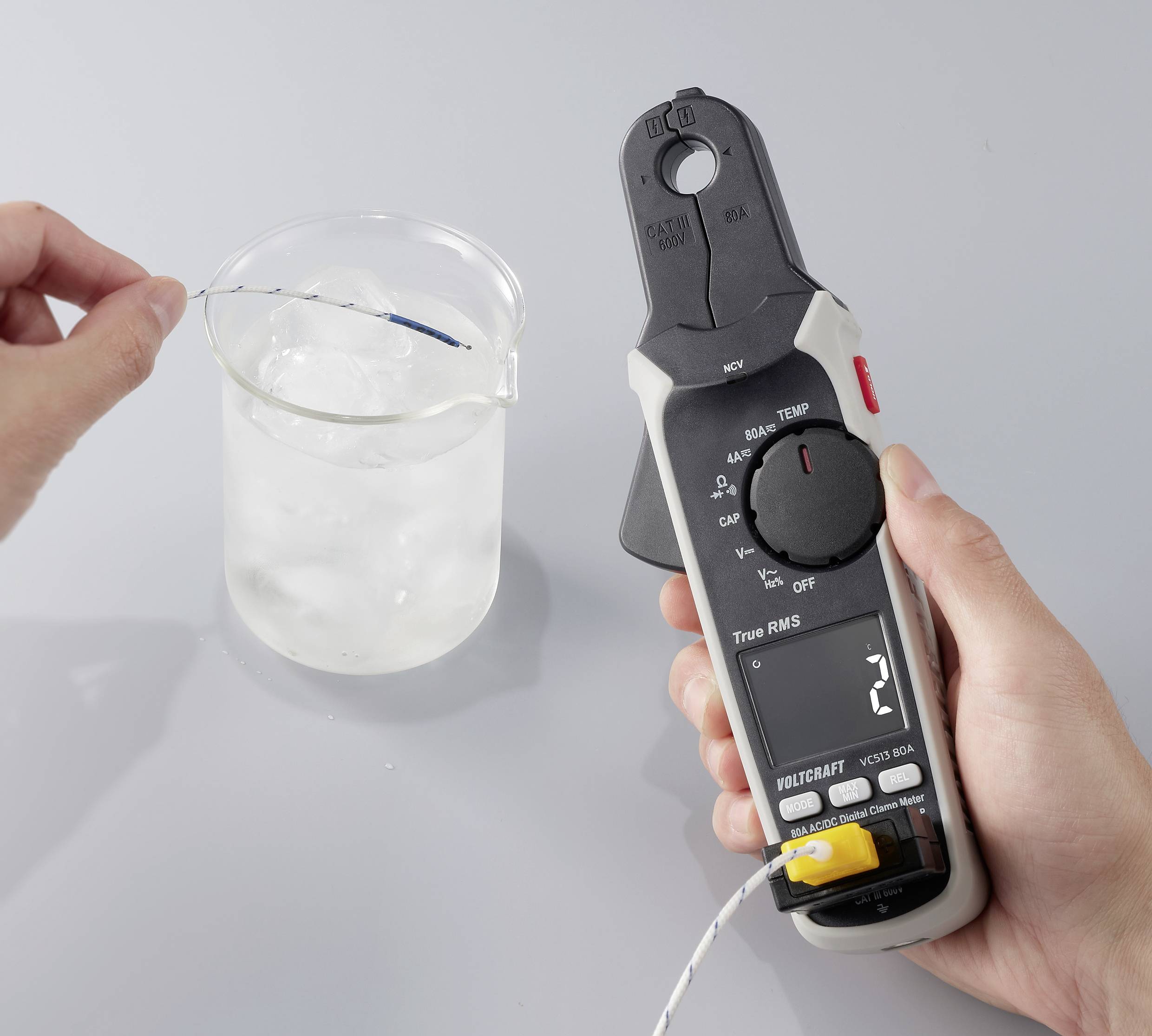 Eine Person verwendet ein digitales Thermometer, um die Temperatur der Flüssigkeit in einem Becherglas zu messen, das mit Eiswasser auf einer grauen Oberfläche gefüllt ist.