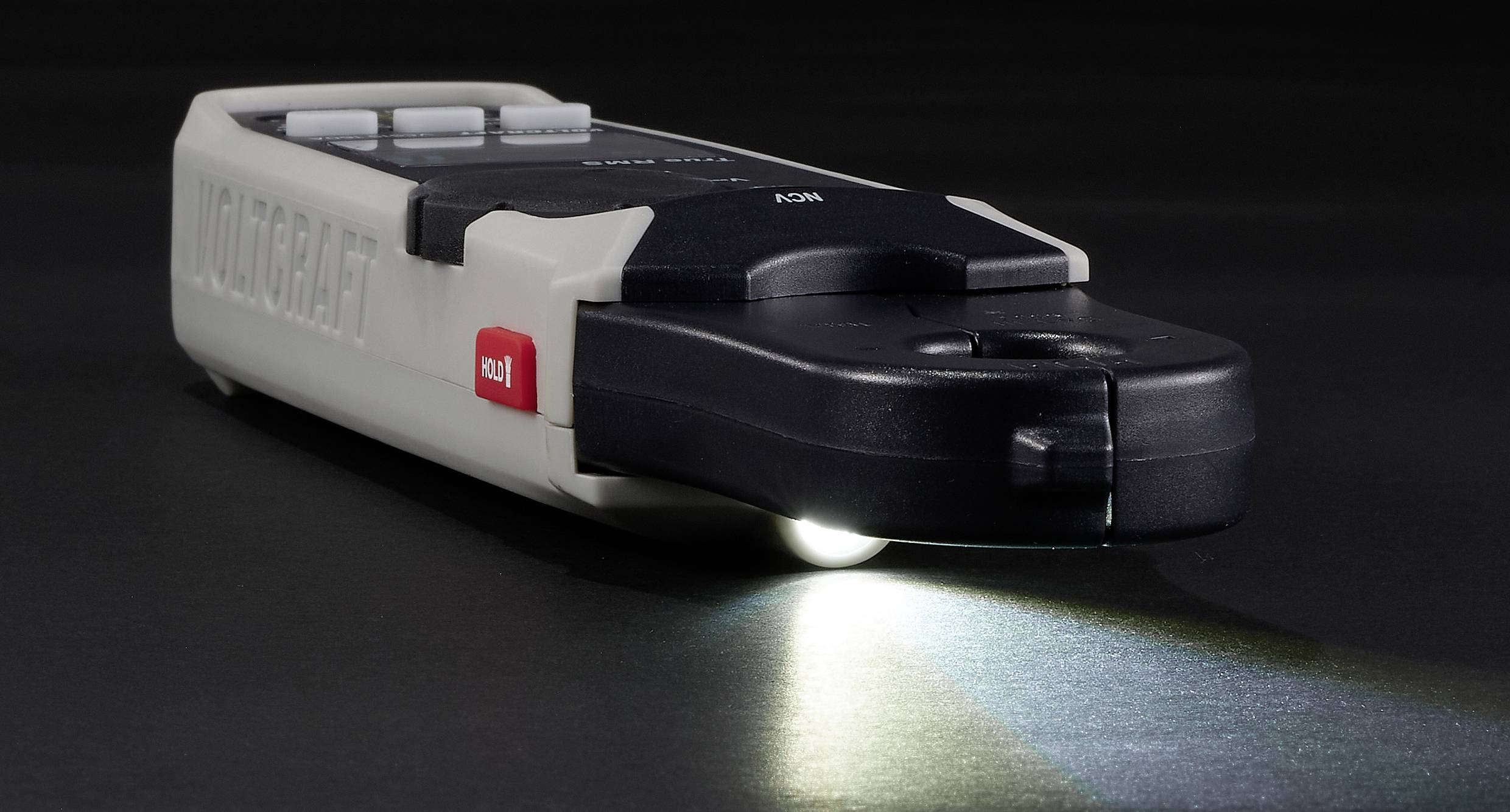 Ein flacher, schwarzer LED-Taschenlampe auf einem Tisch, mit eingeschaltetem Licht. Ein roter Knopf ist auf der Seite sichtbar.