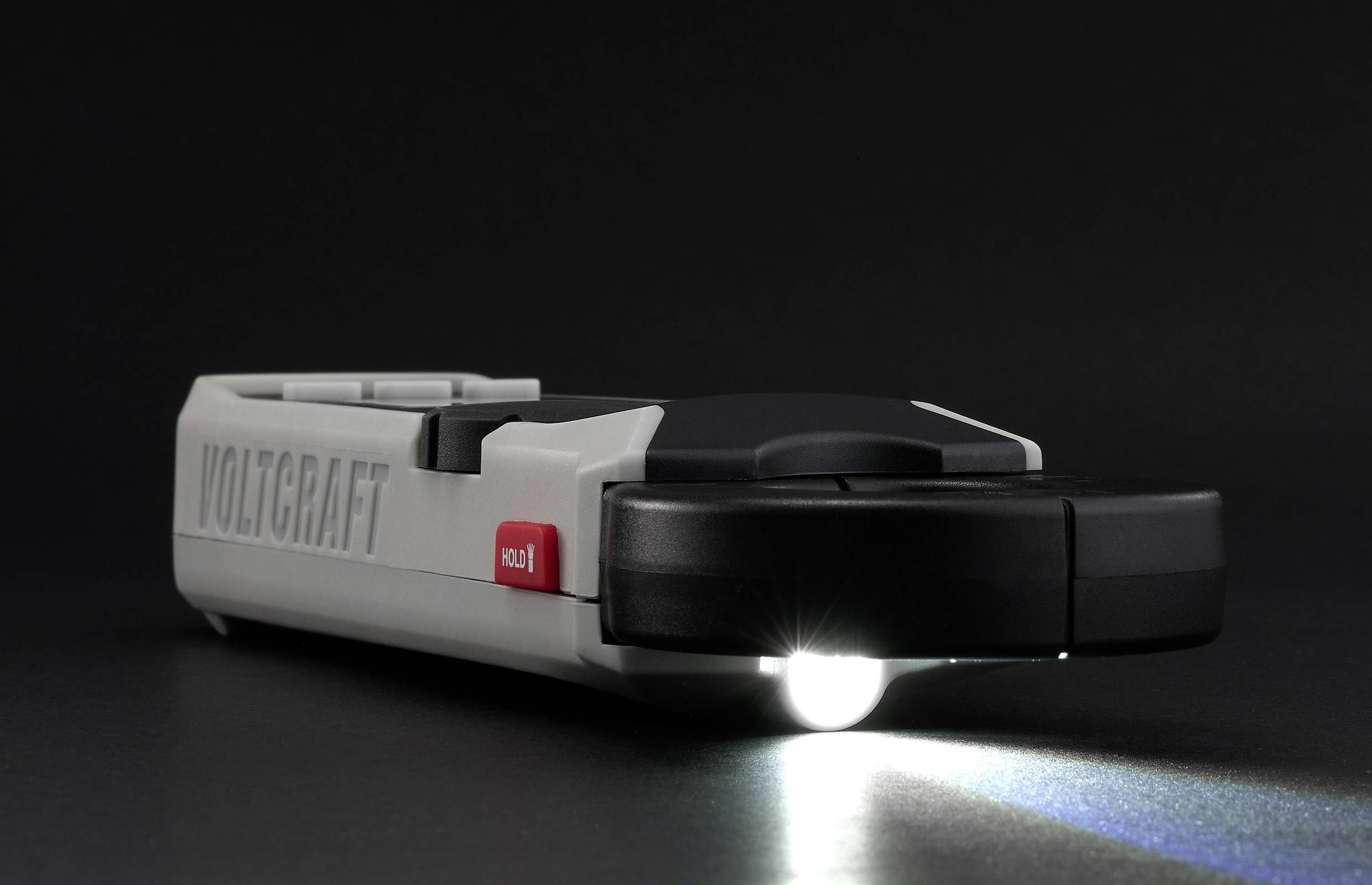 Taschenlampe mit Voltcraft-Logo, eingeschaltet auf dunklem Hintergrund, strahlt Lichtstrahl nach rechts; rote Aus-Taste sichtbar.