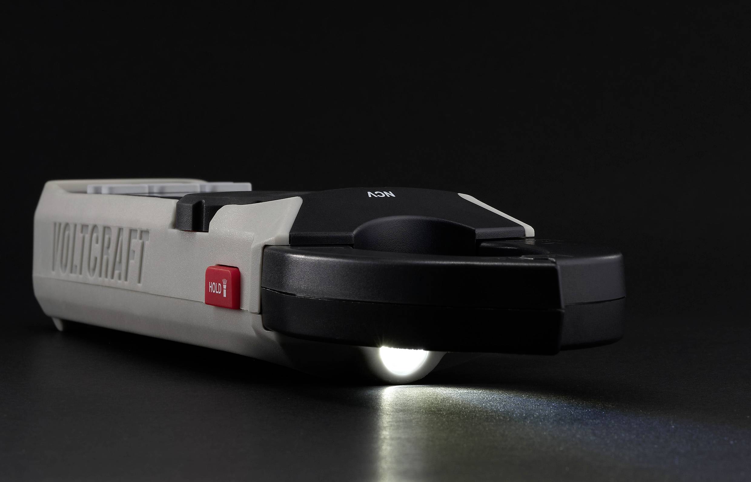 Ein graues Voltmeter von Voltcraft auf einem dunklen Hintergrund, mit einer leuchtenden Taschenlampe am unteren Ende.