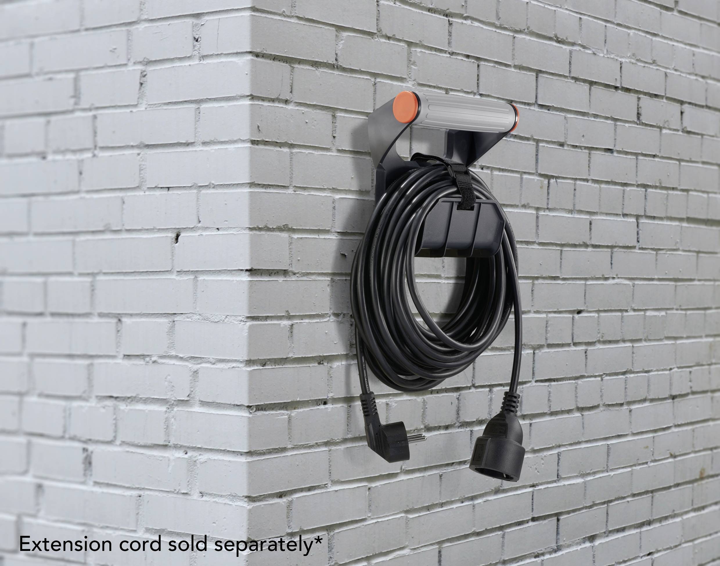 Eine schwarze Kabelaufhängung mit orangenen Akzenten ist an einer weißen Ziegelwand montiert. Ein schwarzes Kabel ist darum gewickelt.