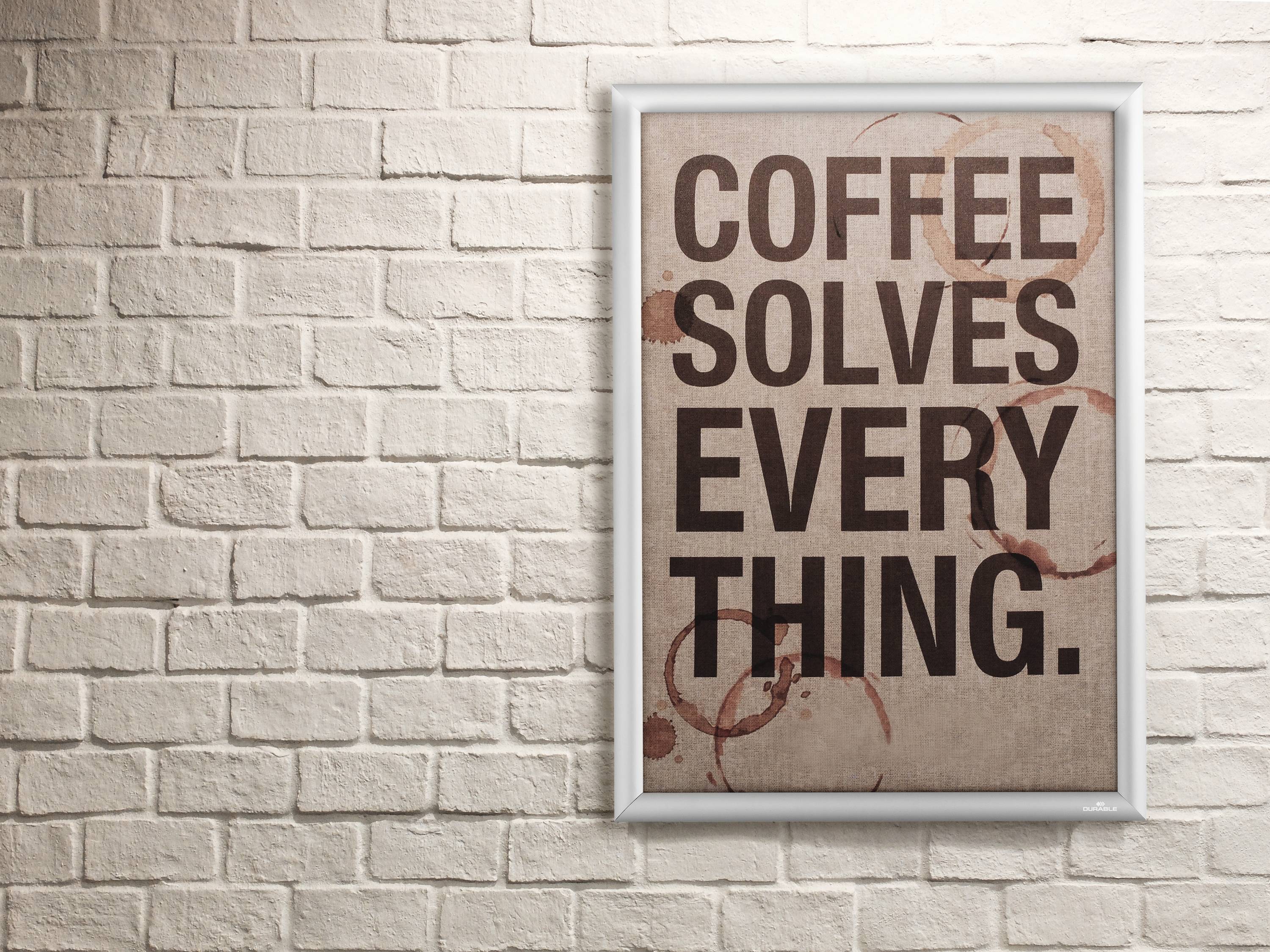 Ein gerahmtes Poster an einer Ziegelwand zeigt den Text 'Coffee Solves Everything' in großen, dunklen Buchstaben.