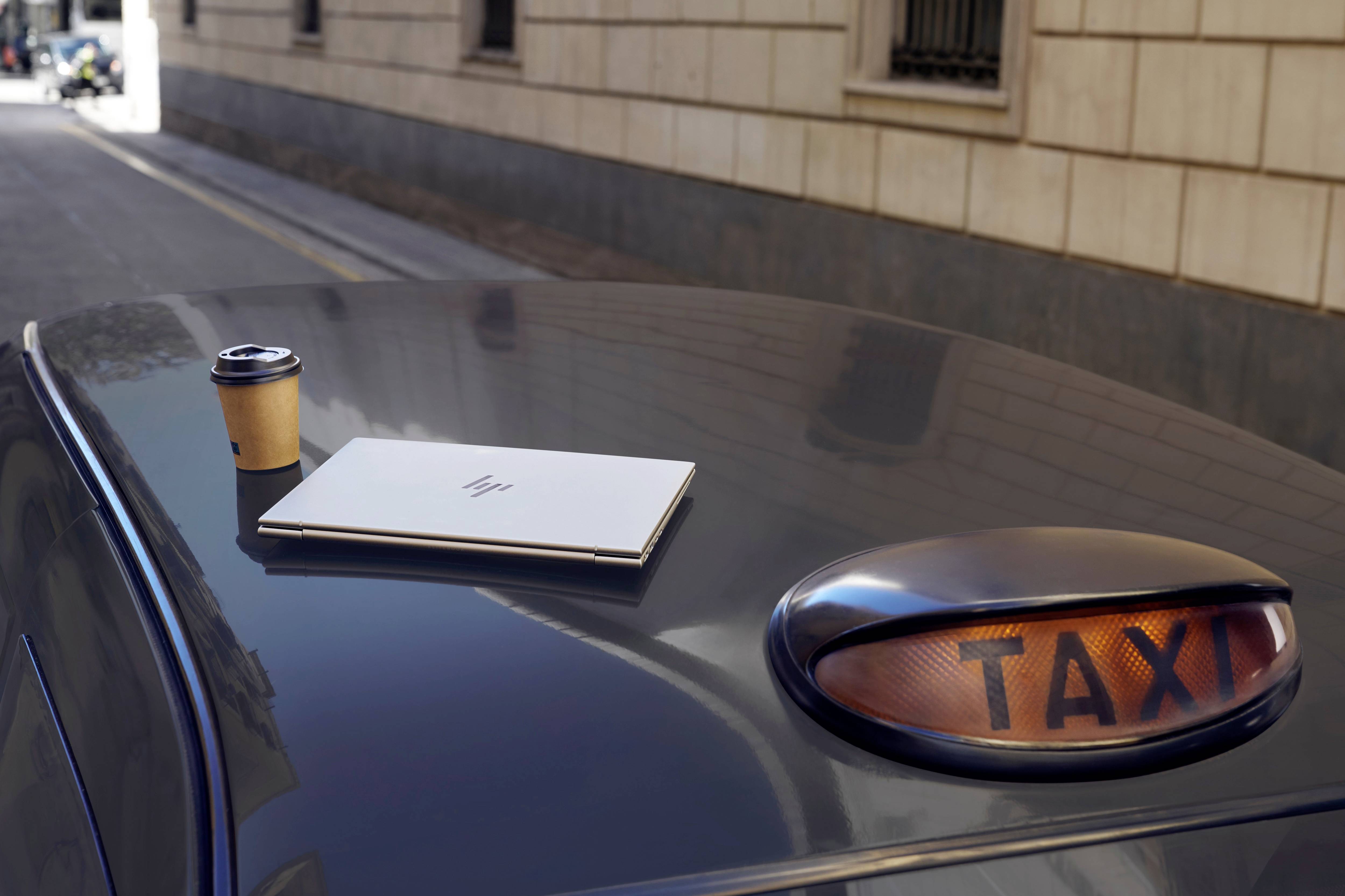 Ein Laptop und ein Kaffeebecher stehen auf dem Dach eines Taxis in einer städtischen Straße.