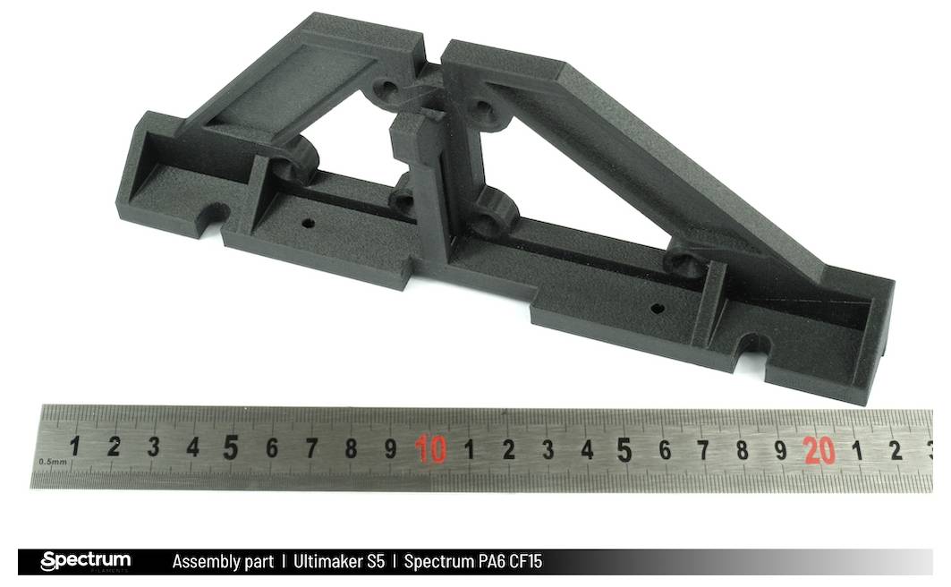 Schwarzes 3D-gedrucktes Bauteil aus speziellem Material neben einem Lineal, das die Größe zeigt. Verwendet für Maschinenbau-Forschung.