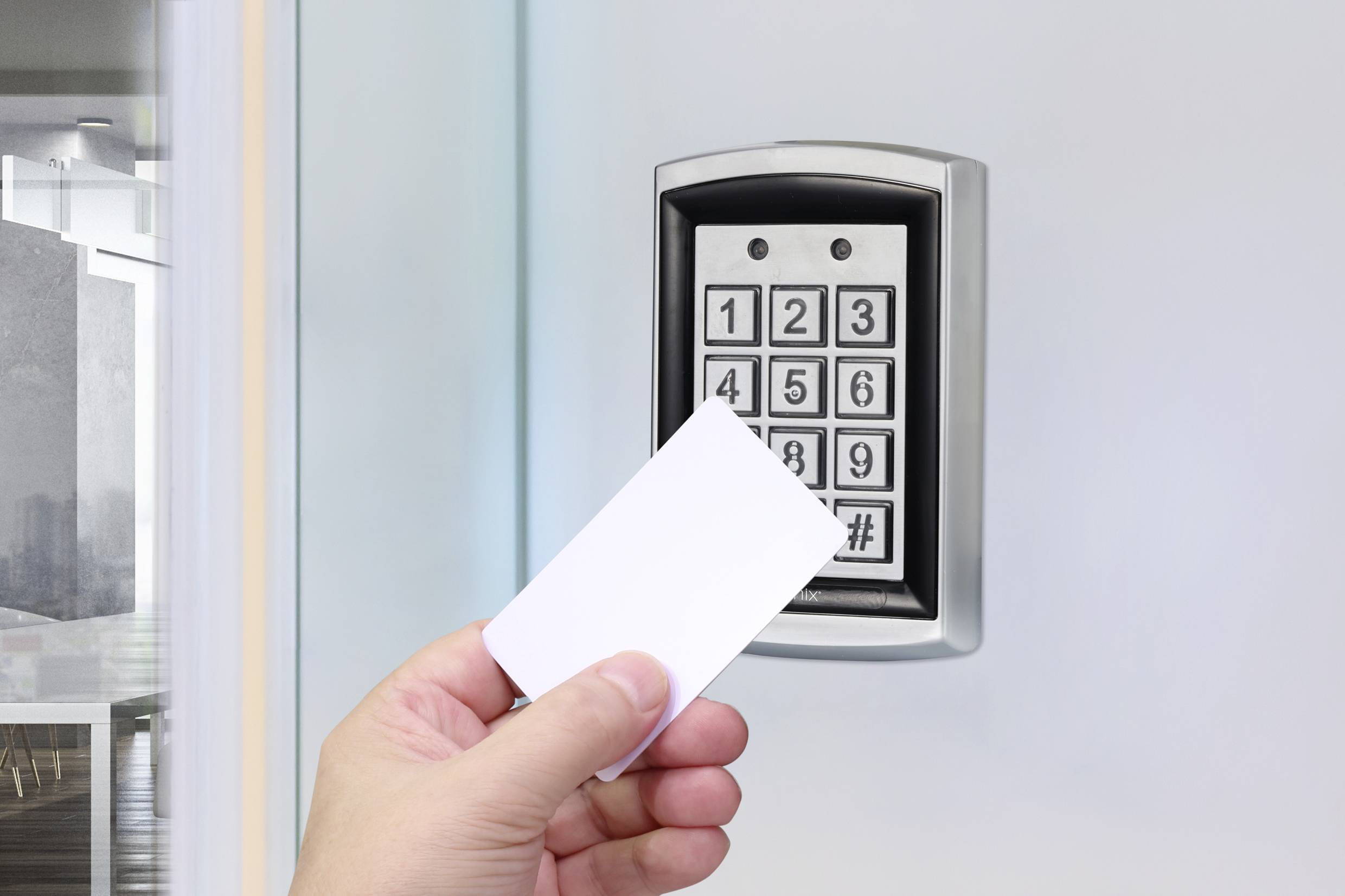 Eine Hand hält eine Karte vor ein elektronisches Zugangskontrollsystem mit Zifferntastatur an einer Glastür.