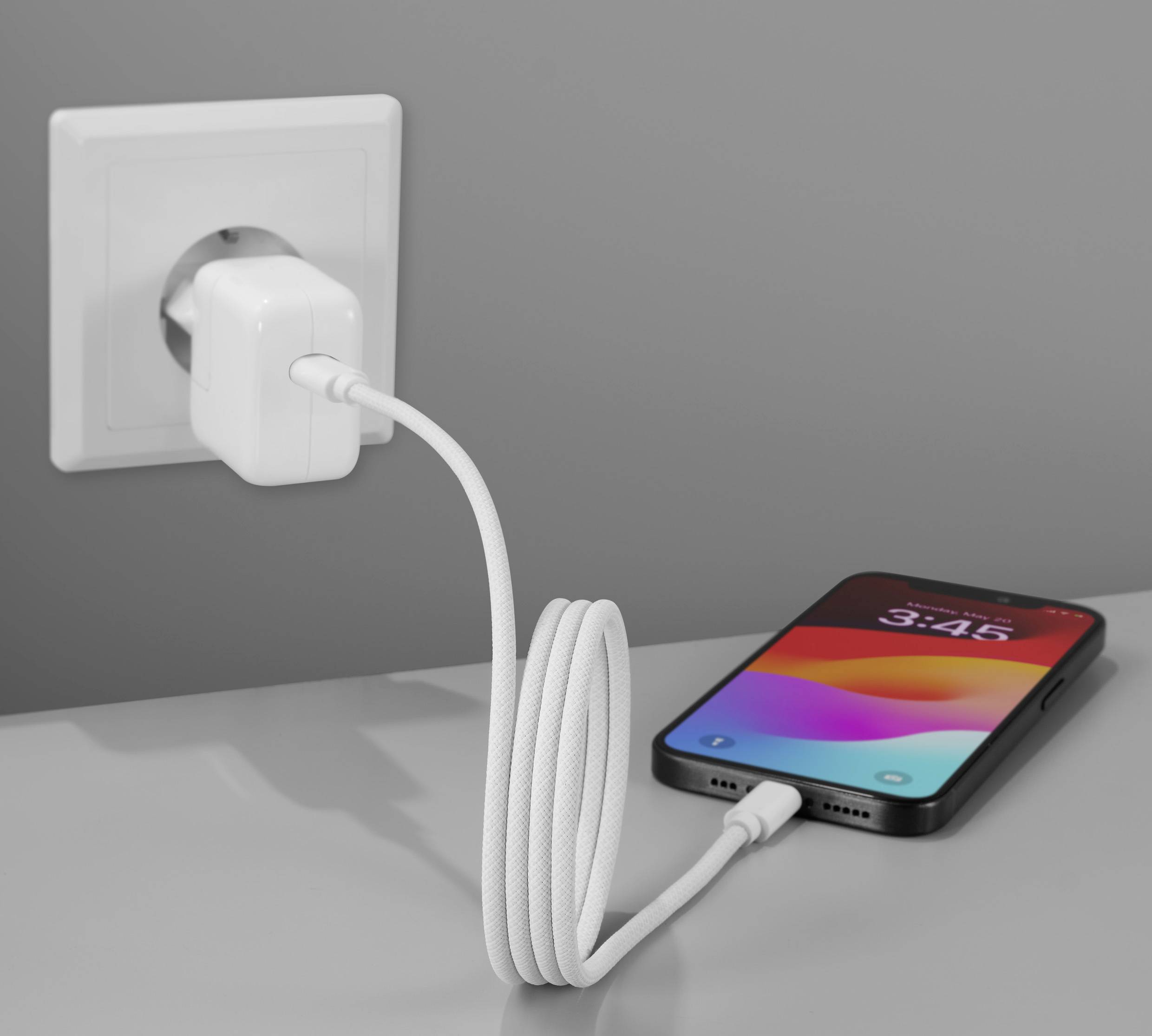 Ein Smartphone wird mit einem Ladekabel an eine Wandsteckdose angeschlossen. Das Display zeigt die Uhrzeit 3:46.