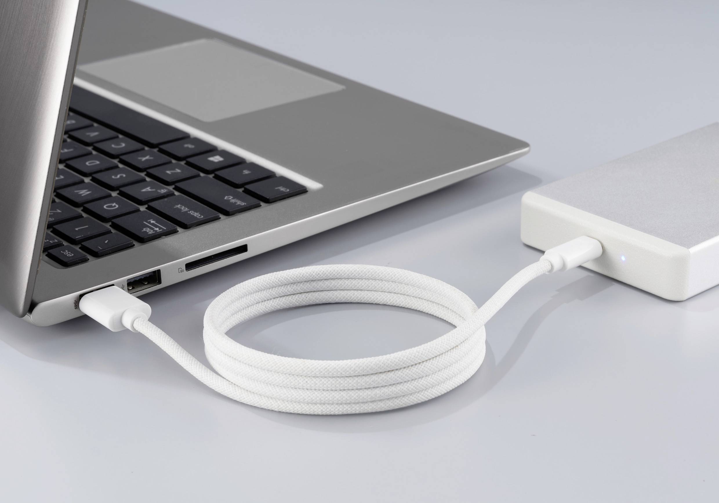 Ein Laptop ist über ein geflochtenes weißes USB-Kabel mit einer externen Festplatte verbunden.