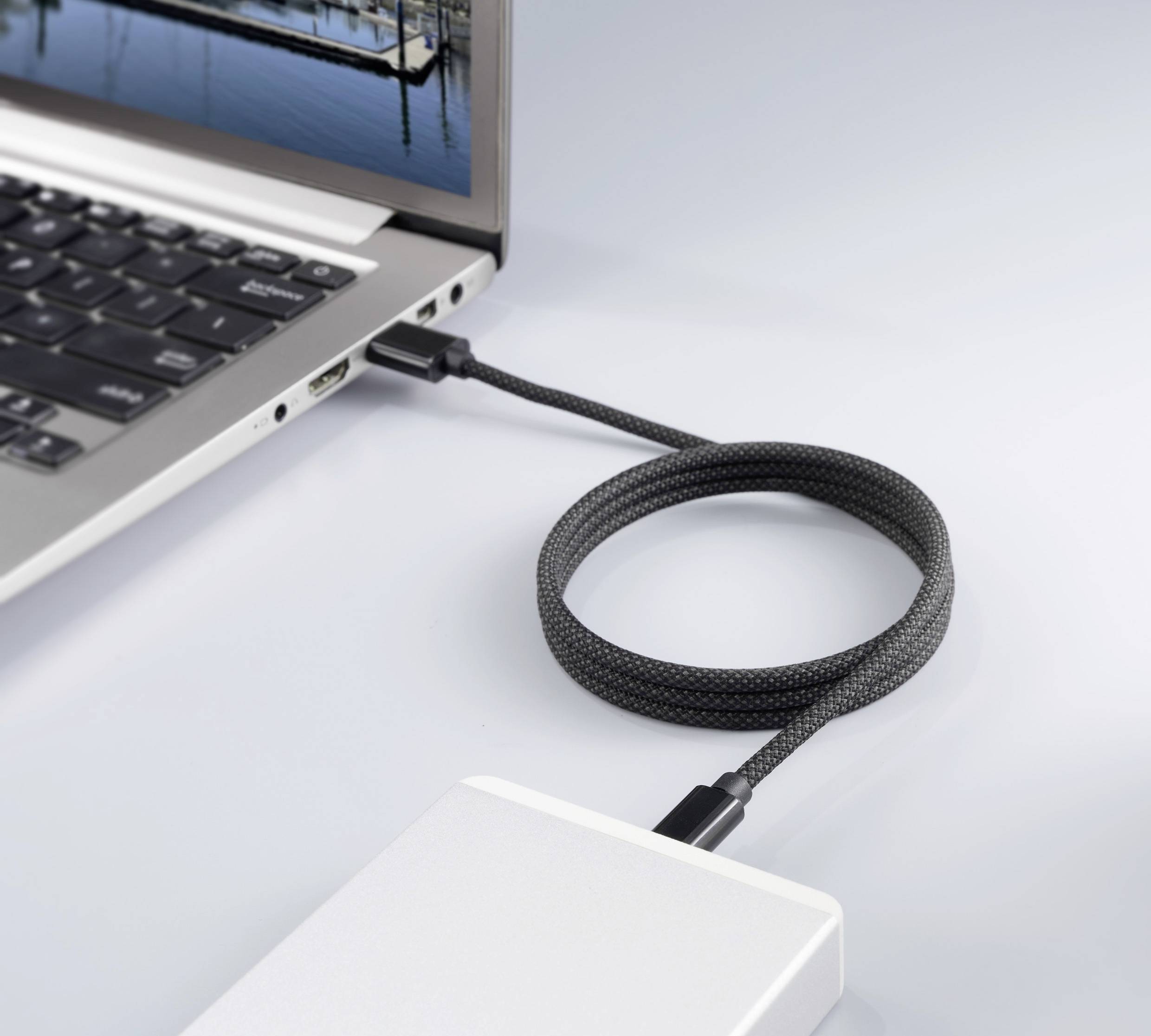 Ein externer Speicher ist über ein Kabel an einen Laptop angeschlossen. Der Laptopbildschirm zeigt ein Bild eines Hafens.