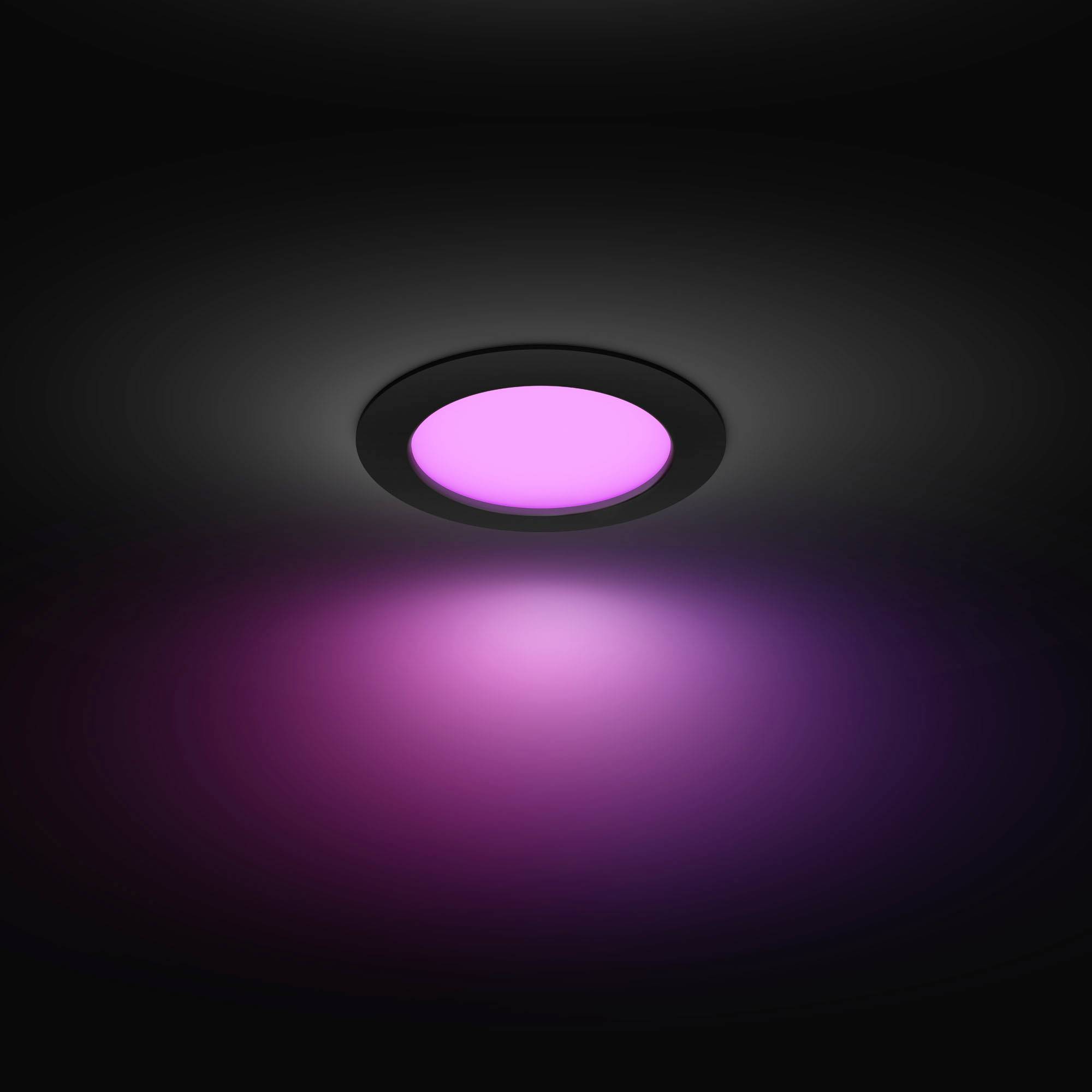 Ein runder Deckenstrahler leuchtet in kräftigem Magenta und wirft einen farbigen Lichtschein auf die dunkle Umgebung.