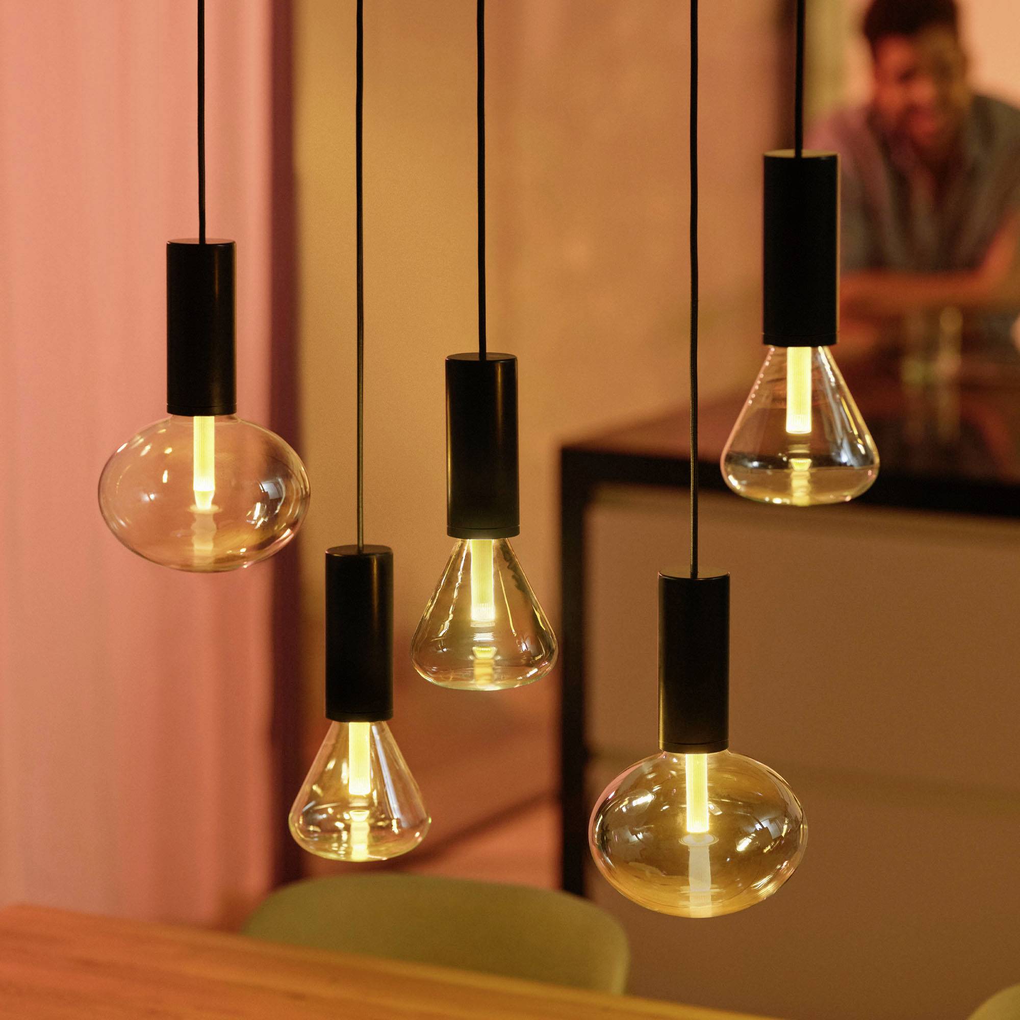 Moderne Hängelampen leuchten warm über einem Tisch. Die Umgebung hat eine gemütliche Atmosphäre mit einem sanften orangenen Licht.