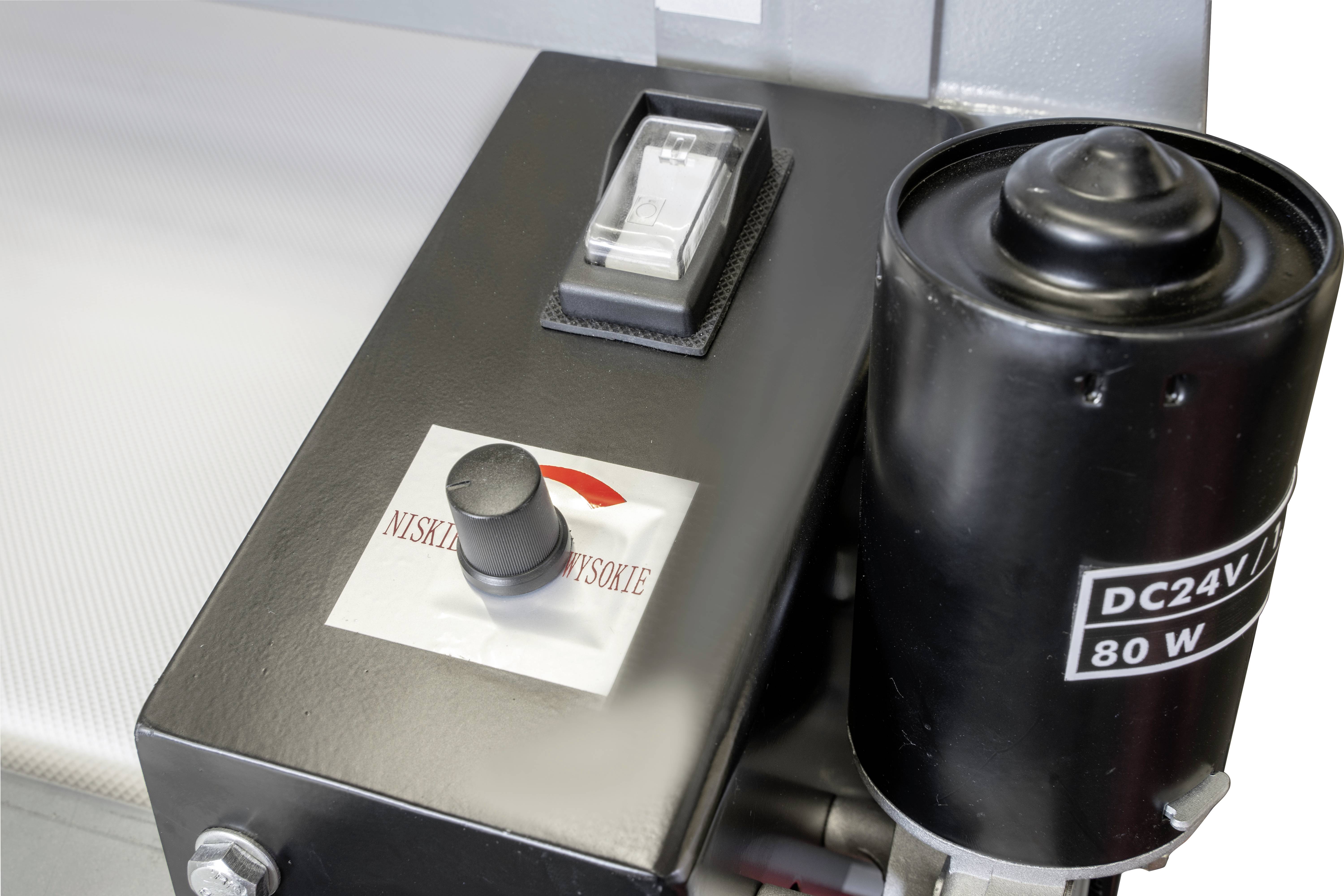 Ein schwarzer Metallzylinder mit der Aufschrift 'DC24V 80W' und ein Steuerkasten mit Schalter und Knopf auf einer Maschine.