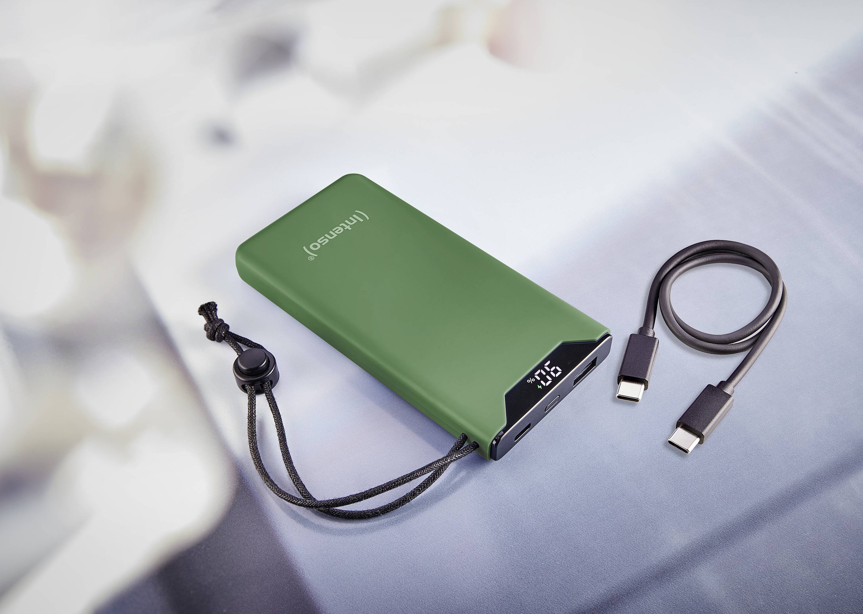 Grüne Powerbank mit digitaler Anzeige zur Batteriekapazität, begleitet von einem USB-Ladekabel auf einer grauen Oberfläche.