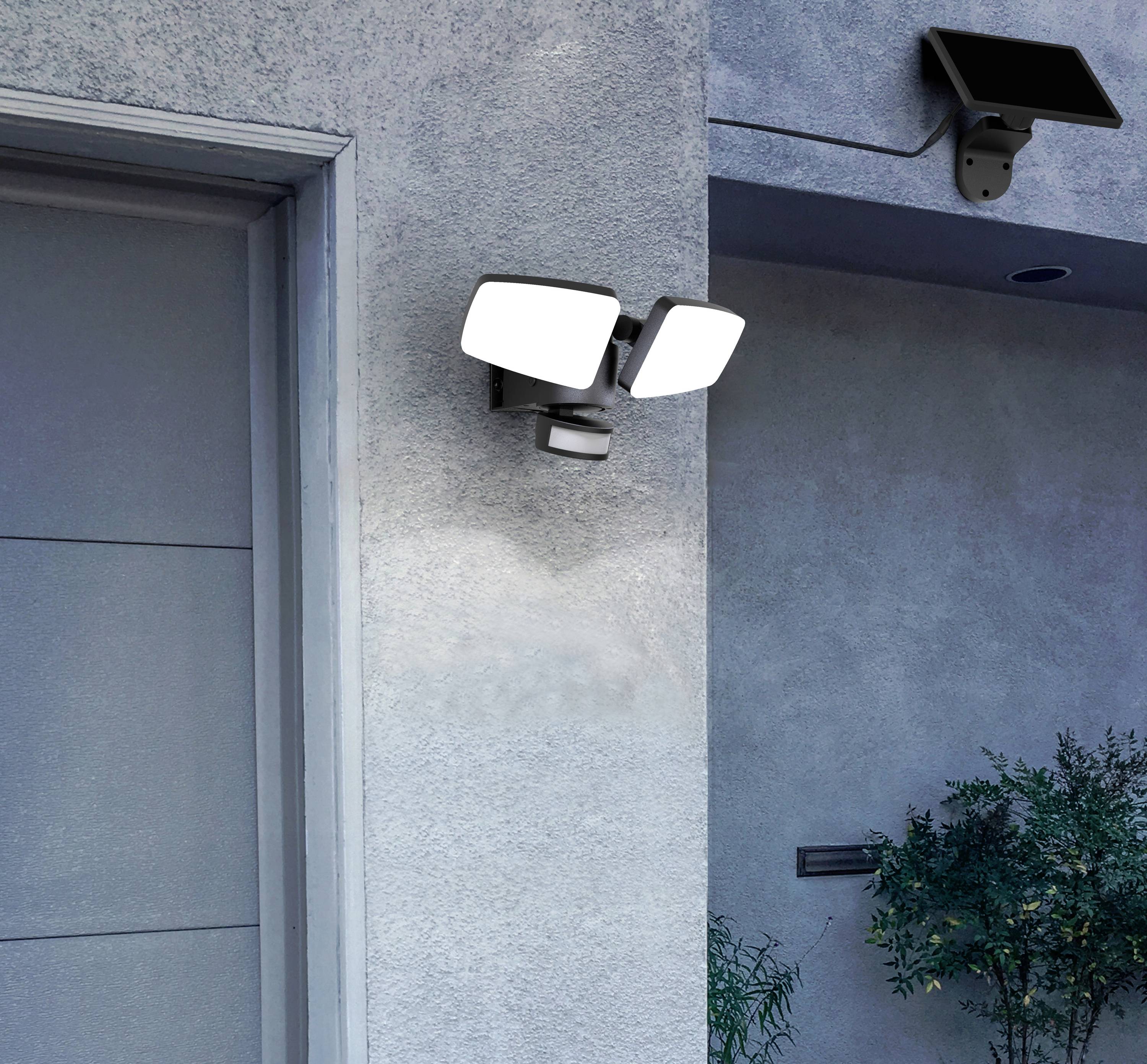 Zwei Außenleuchten an einer grauen Wand eines Hauses. Eine mit zwei quadratischen Paneelen, die andere mit Solarpanel oberhalb der Tür.