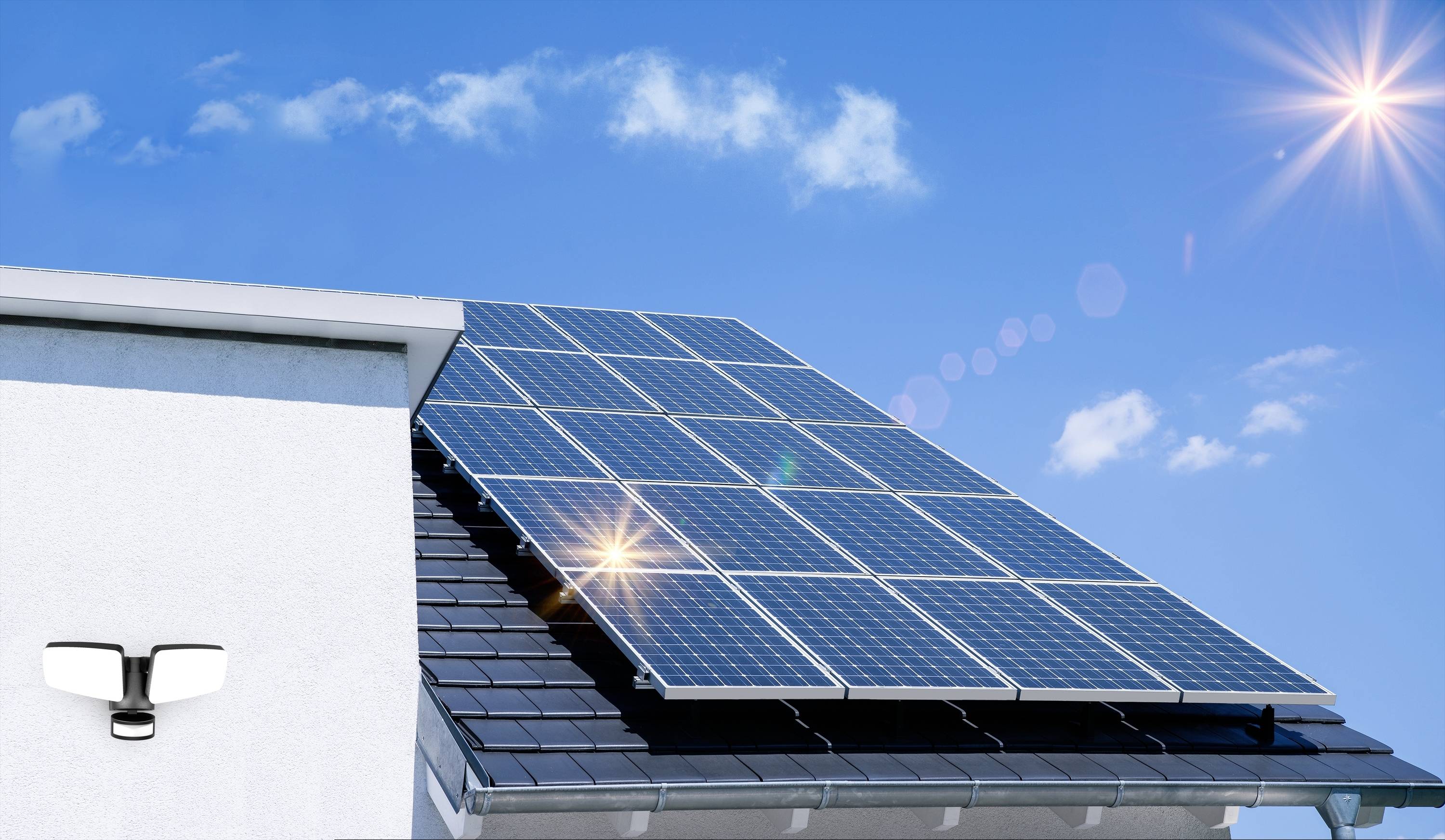 Solaranlage auf einem Hausdach unter strahlend blauem Himmel, Sonnenlicht reflektiert auf den Solarpaneelen.