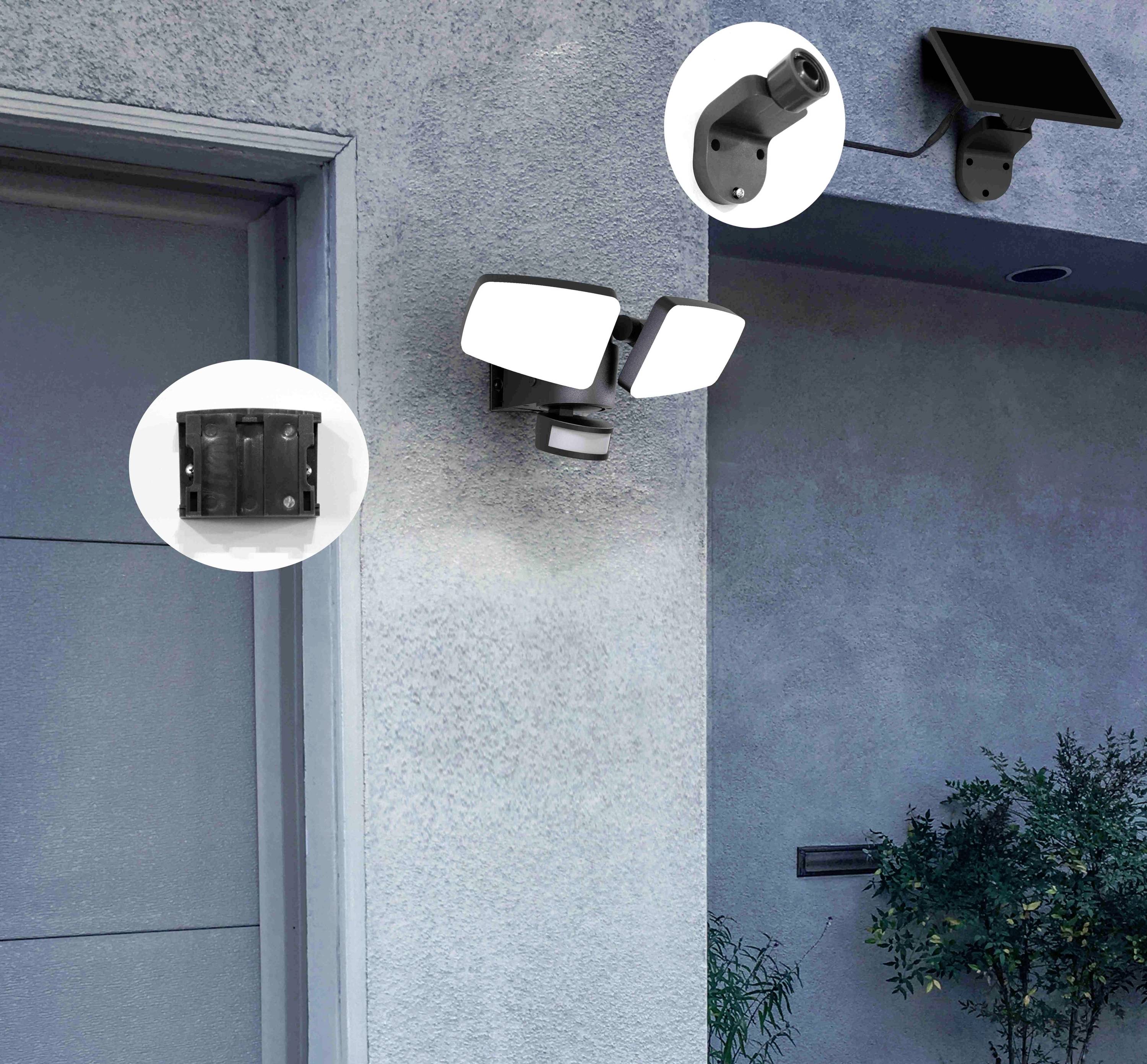 Eine Außenleuchte mit zwei verstellbaren Strahlern und einem Bewegungsmelder ist an der Hauswand neben einer Tür montiert.
