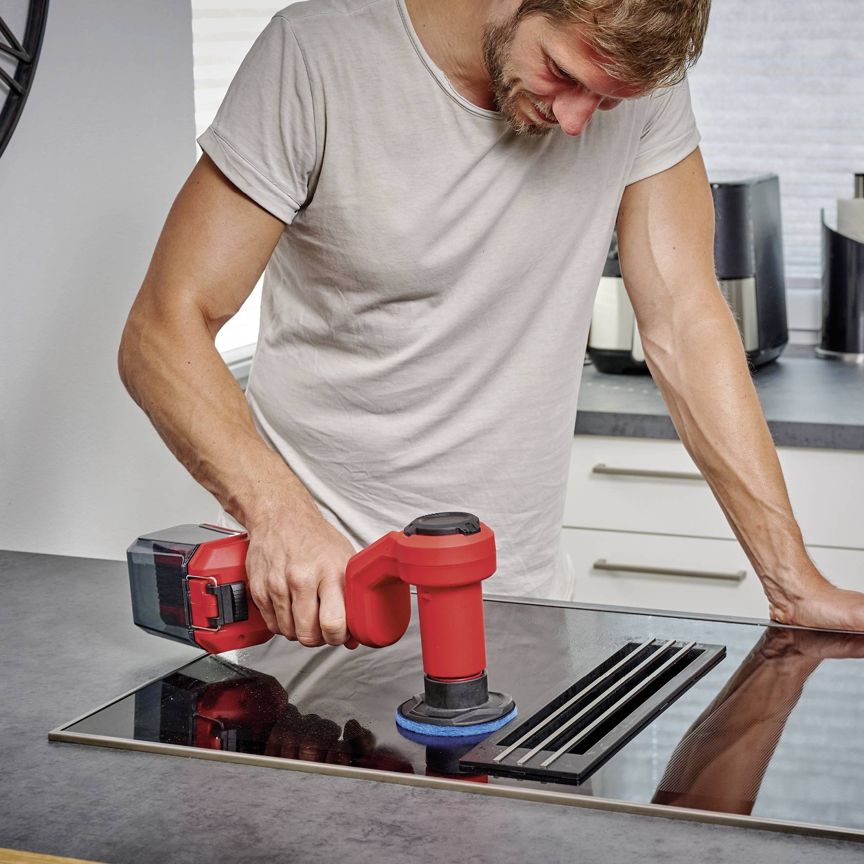Eine Person poliert eine schwarze Induktionskochplatte mit einem roten Poliergerät auf einer Küchentheke.