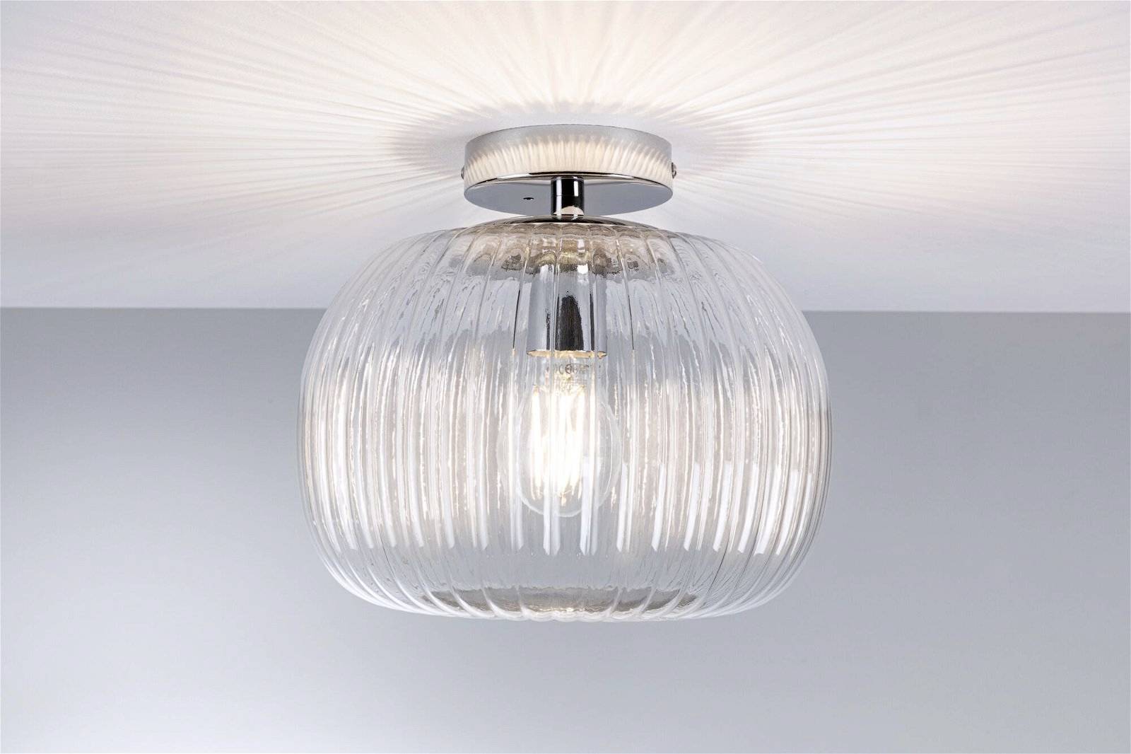 Eine runde Deckenleuchte mit geriffeltem Glas, darunter eine Glühbirne sichtbar. Das Licht strahlt gleichmäßig an die Decke.