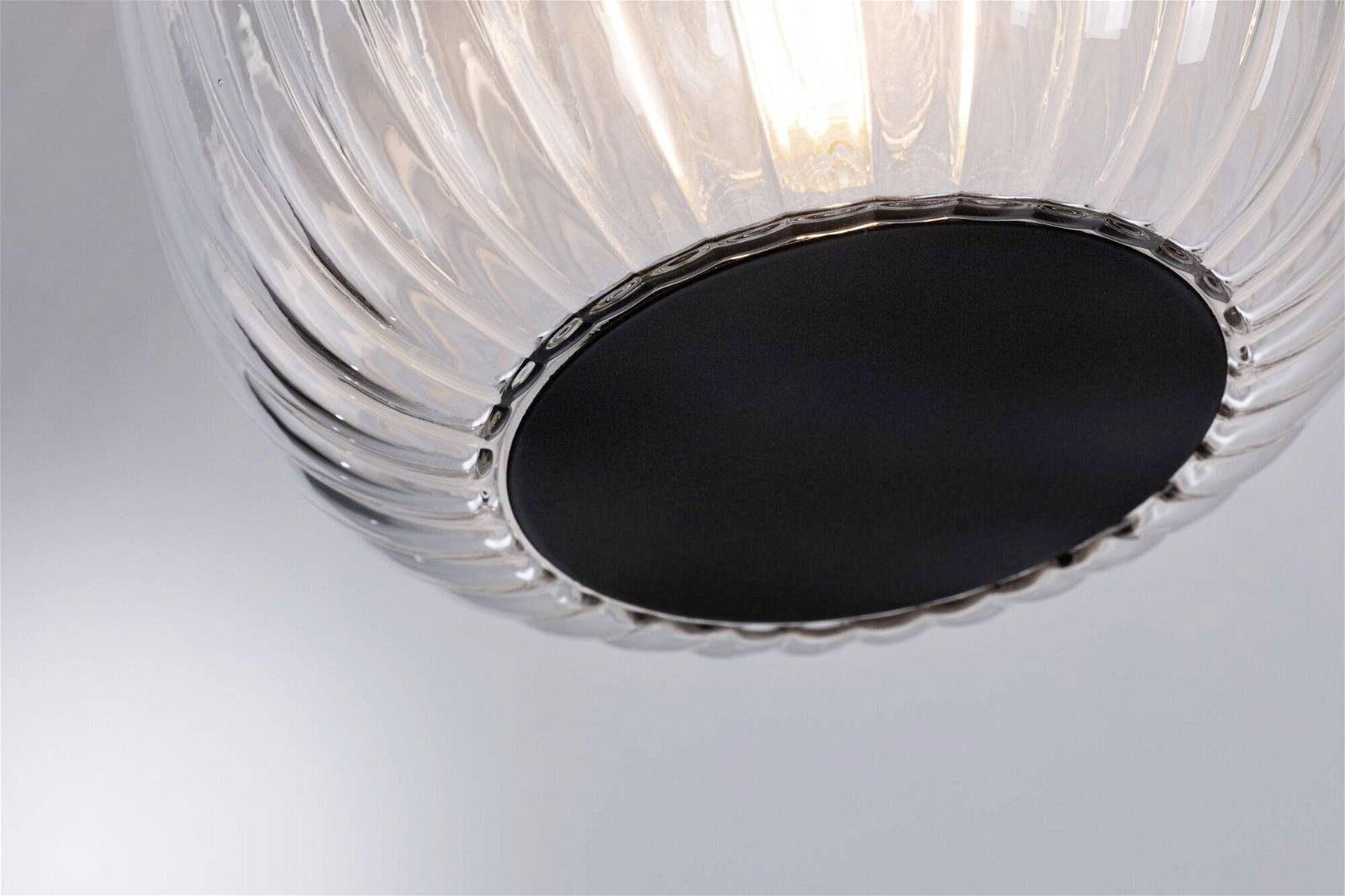 Eine nahaufnahme einer modernen Leuchte mit transparentem, geriffeltem Glas und schwarzem Metallsockel. Sie strahlt ein warmes Licht aus.