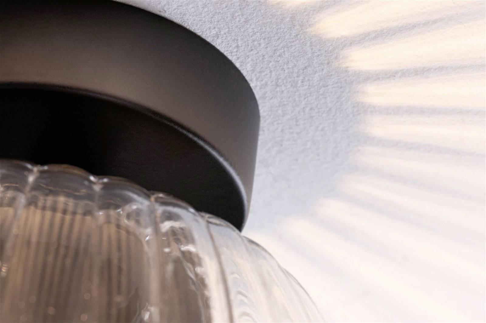 Runde Deckenleuchte mit glasartigem Lampenschirm, wirft gleichmäßige Lichtstreifen an die weiße Decke, moderne Atmosphäre.