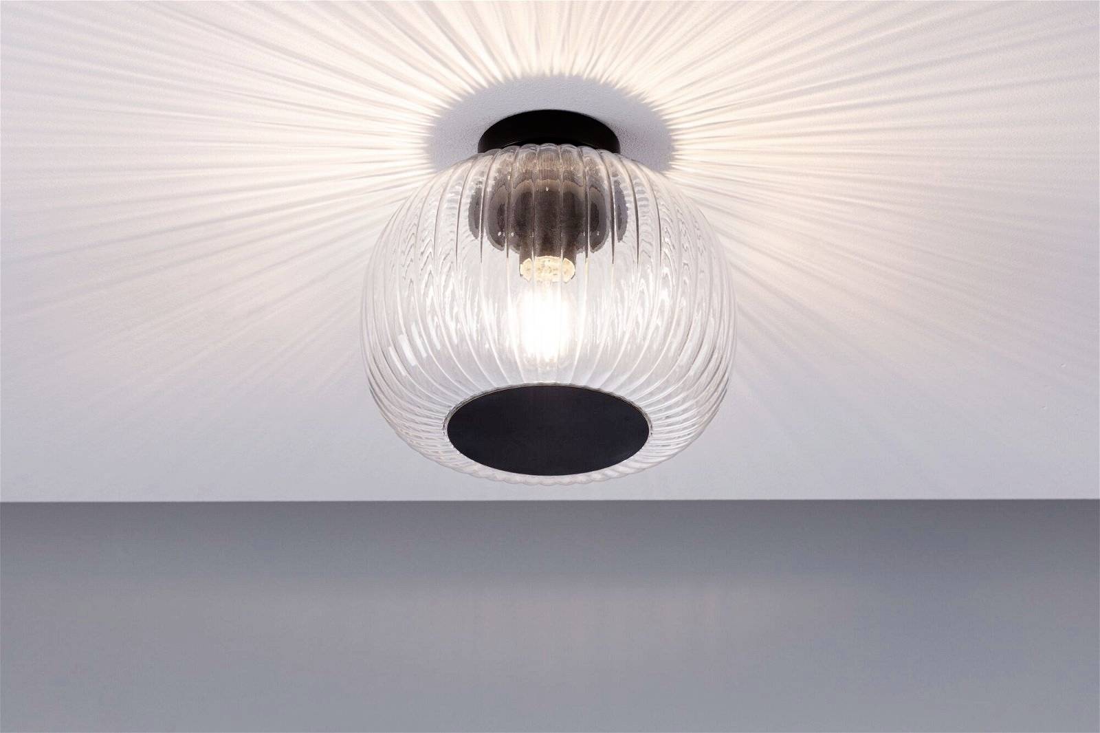 Nahaufnahme einer modernen Deckenleuchte mit geriffeltem Glaskörper und sichtbarer Glühbirne. Sie strahlt weiches Licht in den Raum.