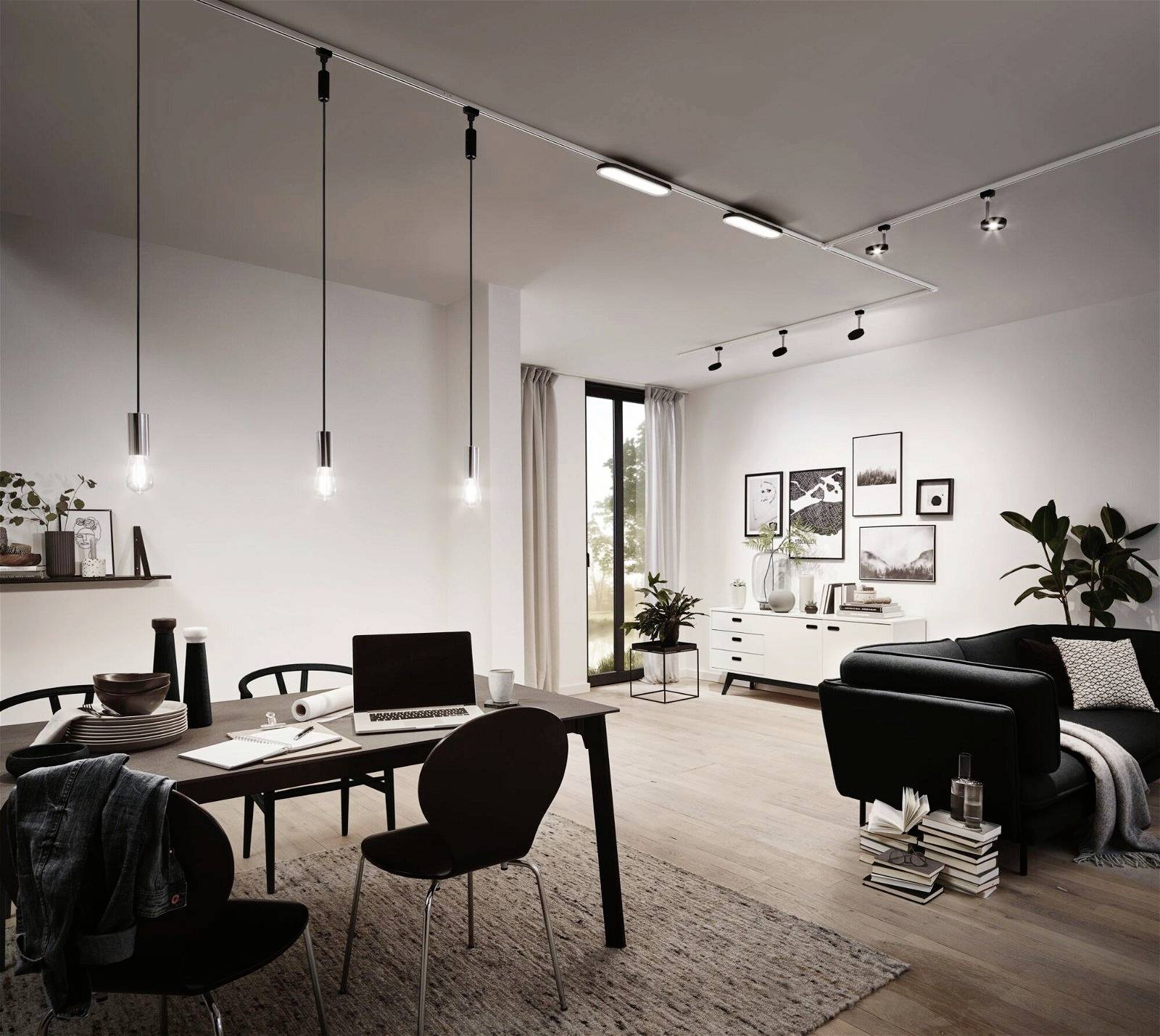 Modernes Wohnzimmer mit Esstisch, an dem ein Laptop steht. Helle Wände, schlichte Hängelampen, Sofa und Dekoration vermitteln ein minimalistisches Design.