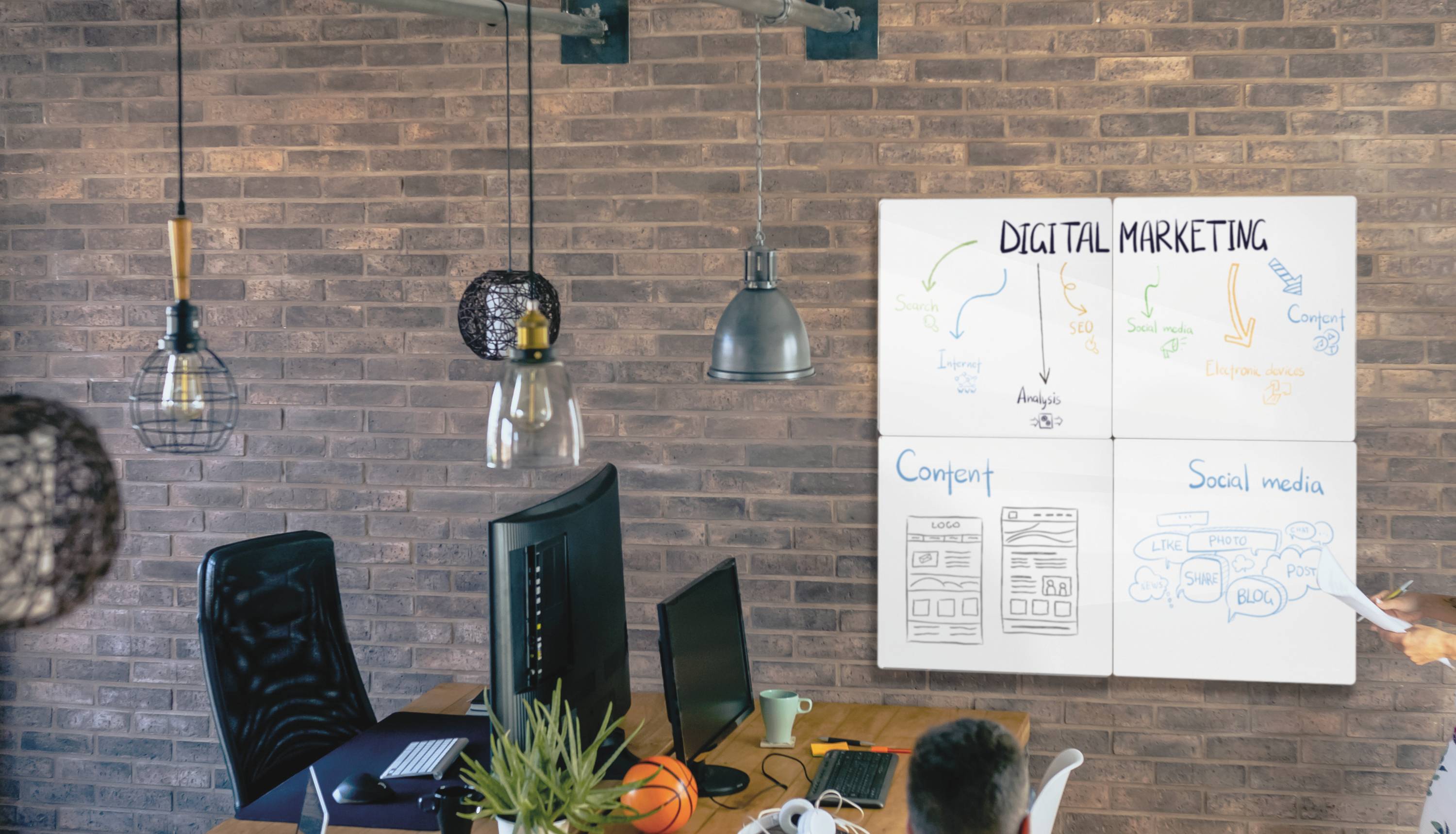 Ein Büro mit zwei Personen, die an Computern arbeiten. An der Wand hängen Tafeln mit Diagrammen und Texten zum Thema 'Digital Marketing'.