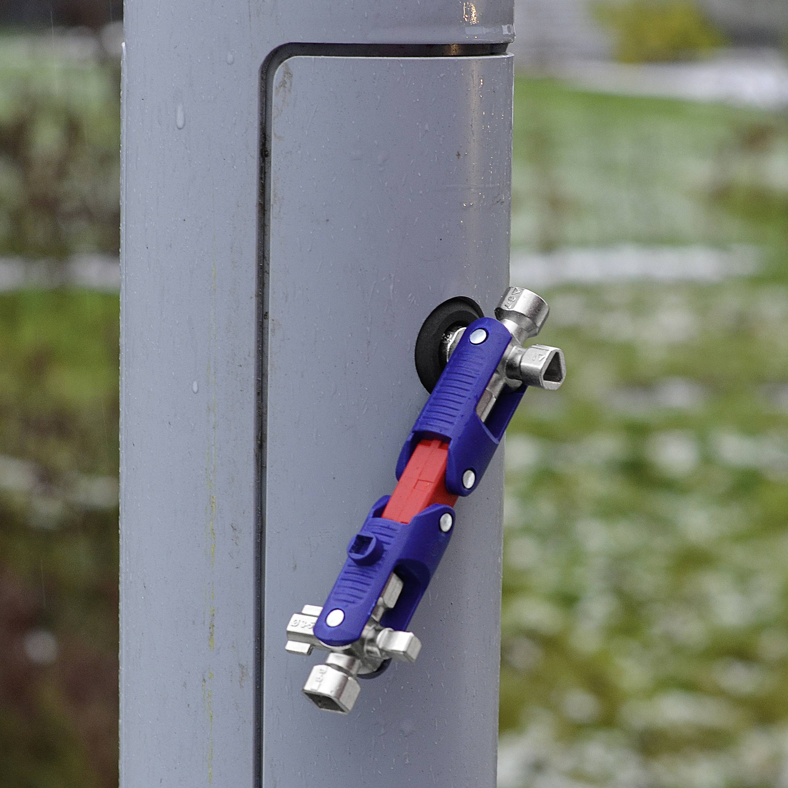 Blauer Bügelschloss geöffnet an einem grauen Metallpfosten befestigt. Unscharfer Hintergrund mit grünem Gras.