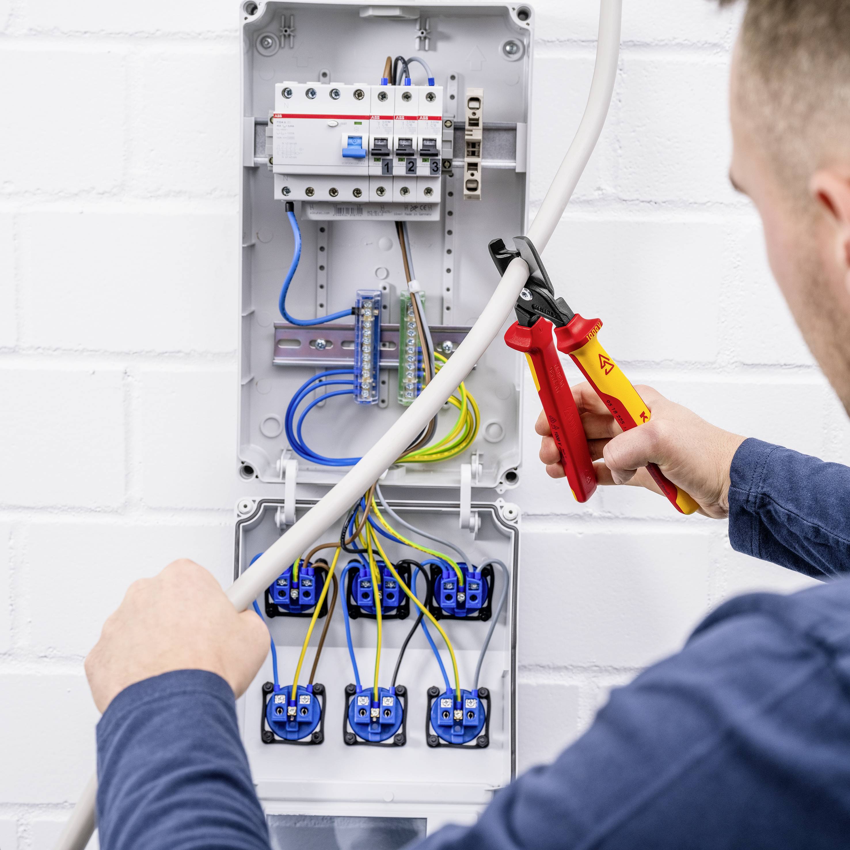 Ein Elektriker arbeitet an einem Sicherungskasten. Er verwendet ein Crimpwerkzeug, um Kabel zu verbinden.