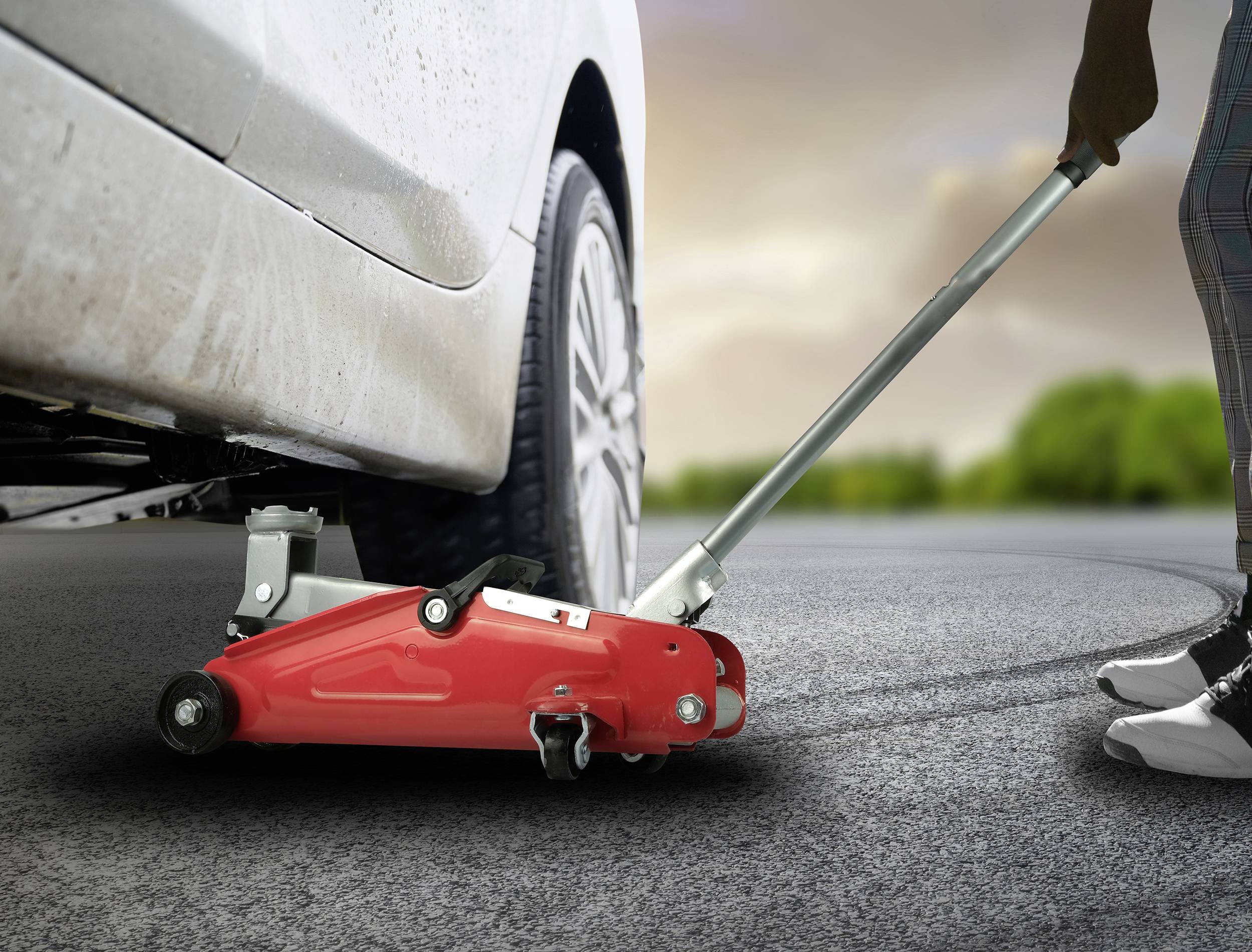 Eine Person benutzt einen Wagenheber, um ein Auto anzuheben. Der Wagenheber ist rot und befindet sich unter dem Auto.