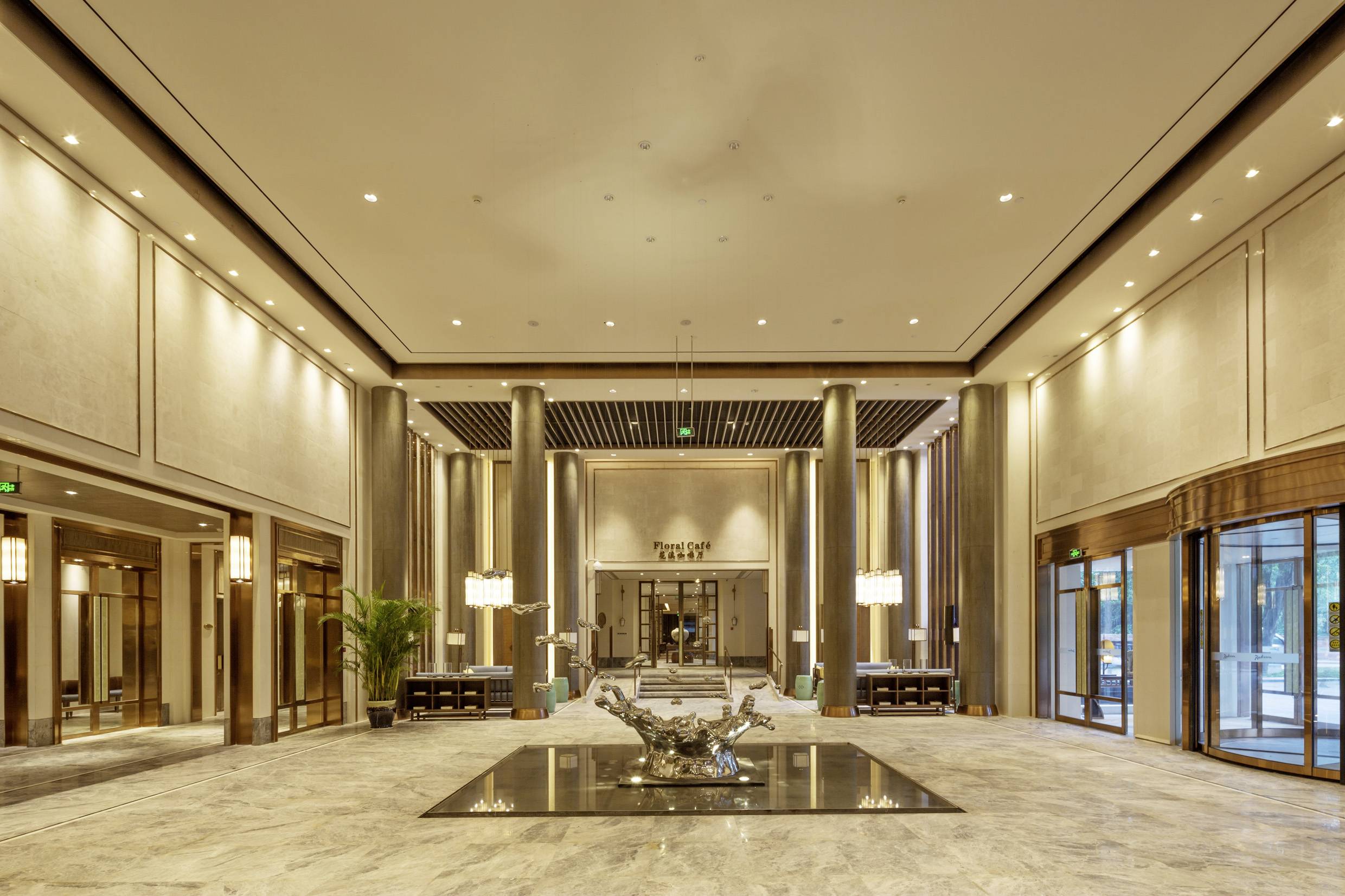 Geräumige Hotellobby mit eleganten, modernen Designs. Große Kronleuchter hängen von der Decke, kunstvolle Skulptur im Zentrum.