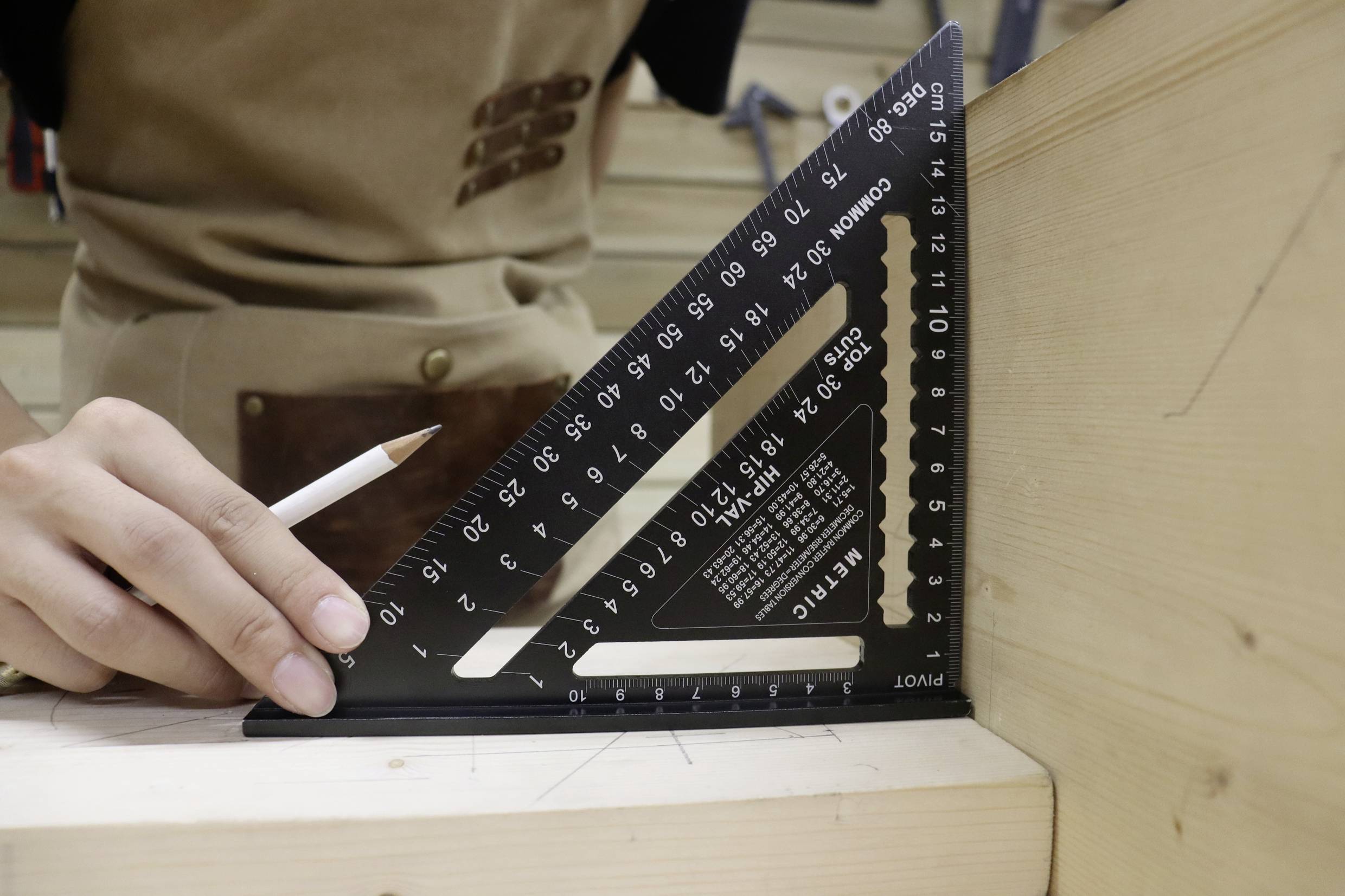 Eine Person misst mit einem schwarzen Winkelmesser auf einem Holzbrett, hält einen Bleistift in der Hand.