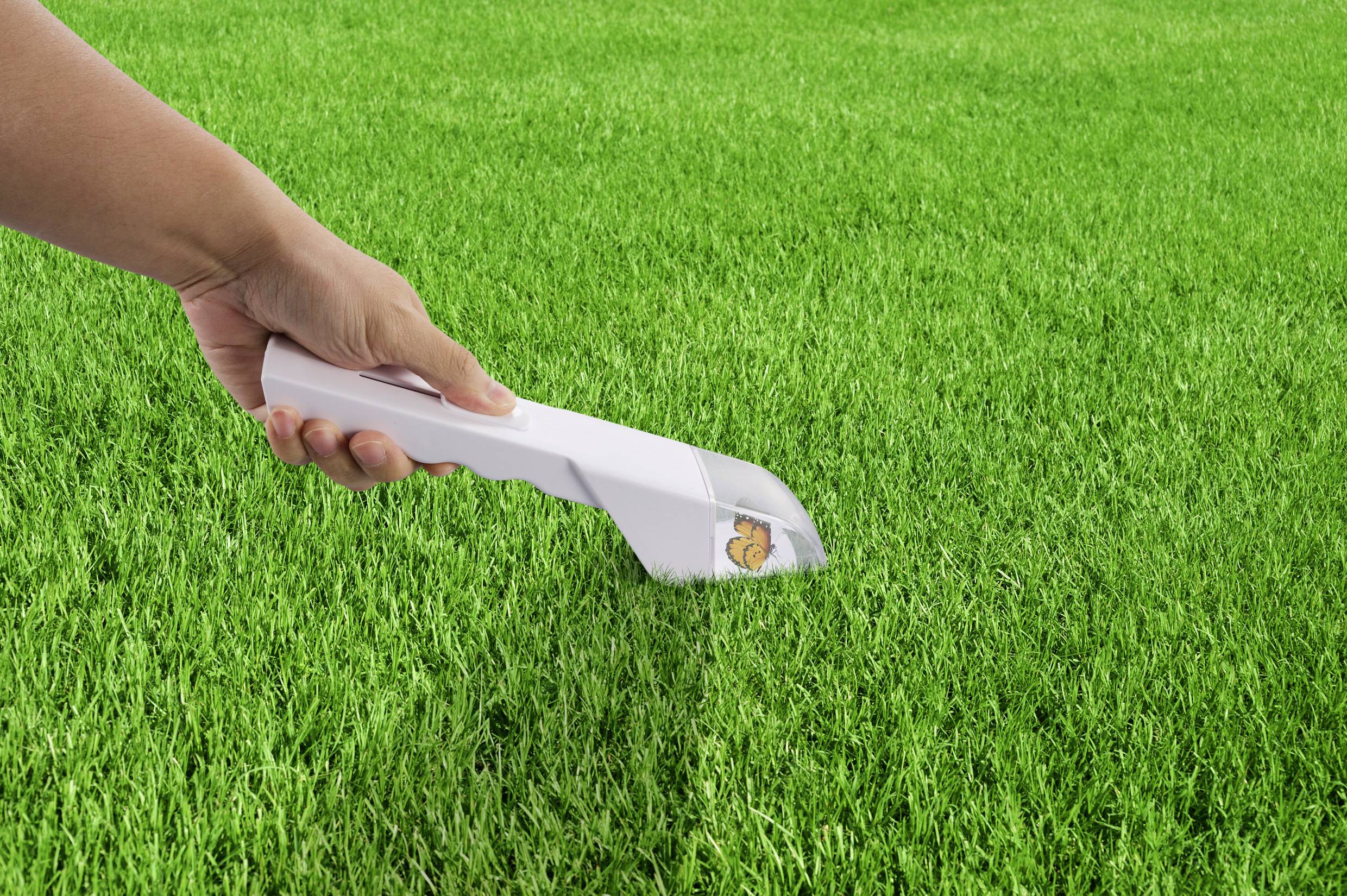 Eine Hand hält einen Staubsauger, der über grünes Gras geführt wird.