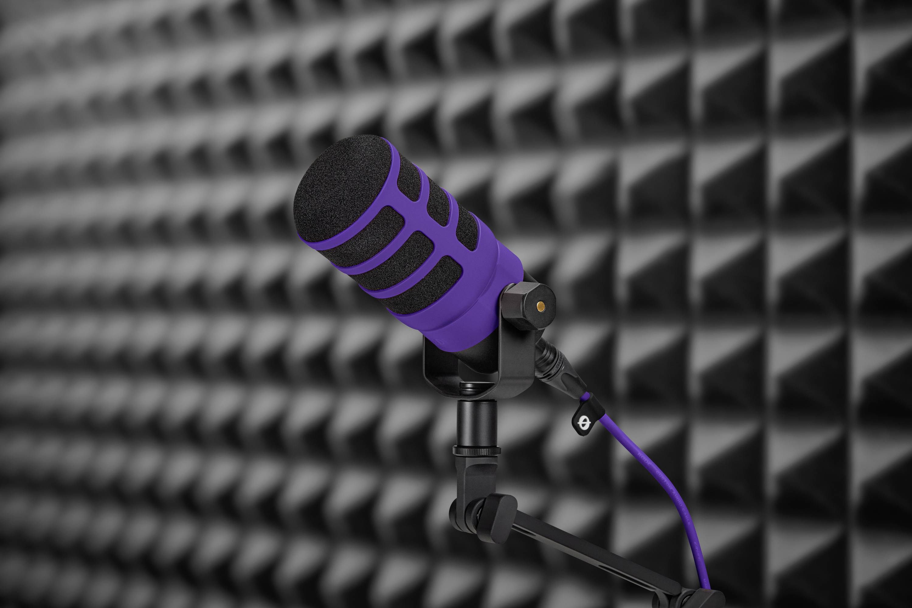 Lila Mikrofon auf einem Ständer vor schallisolierter Wand, bereit für Aufnahmen oder Podcasts.